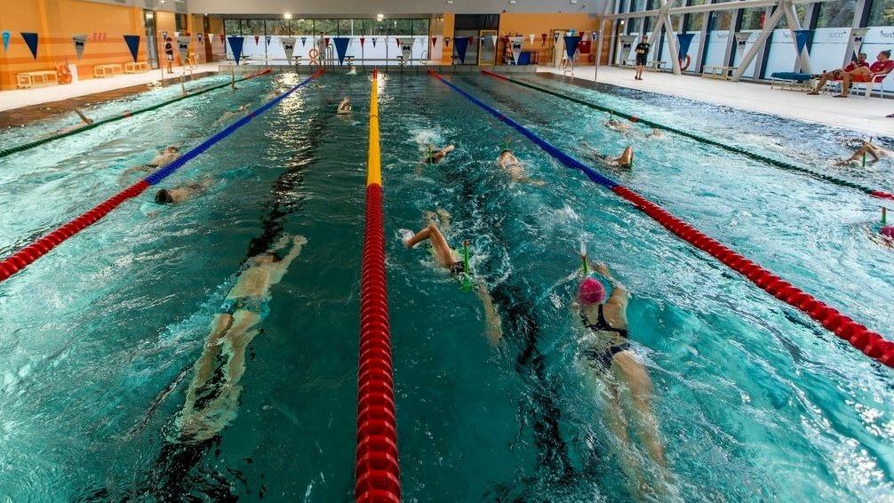 Wnętrze basenu, na pierwszym planie pływacy, z boku widać ratowników