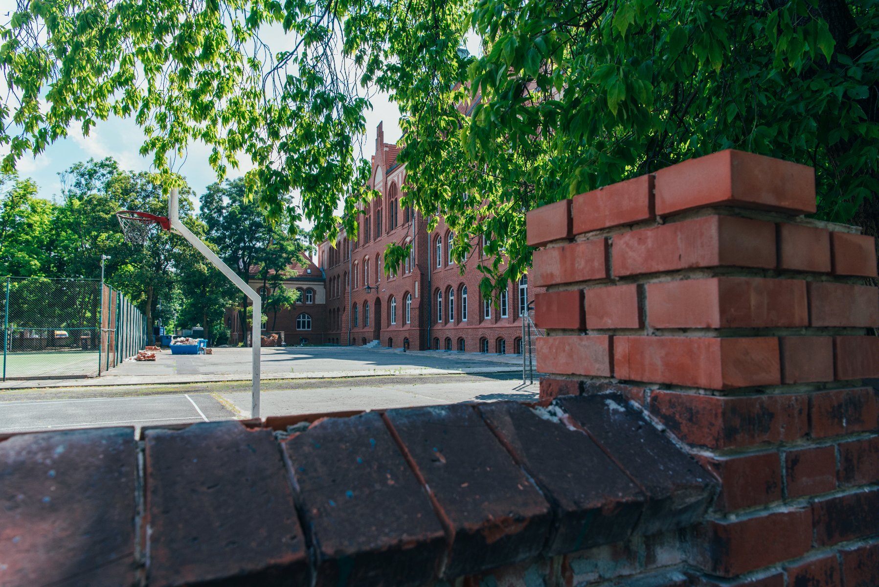 Zdjęcie przedstawia budynek szkoły, na pierwszym planie znajduje się betonowe ogrodzenie. - grafika rozmowy