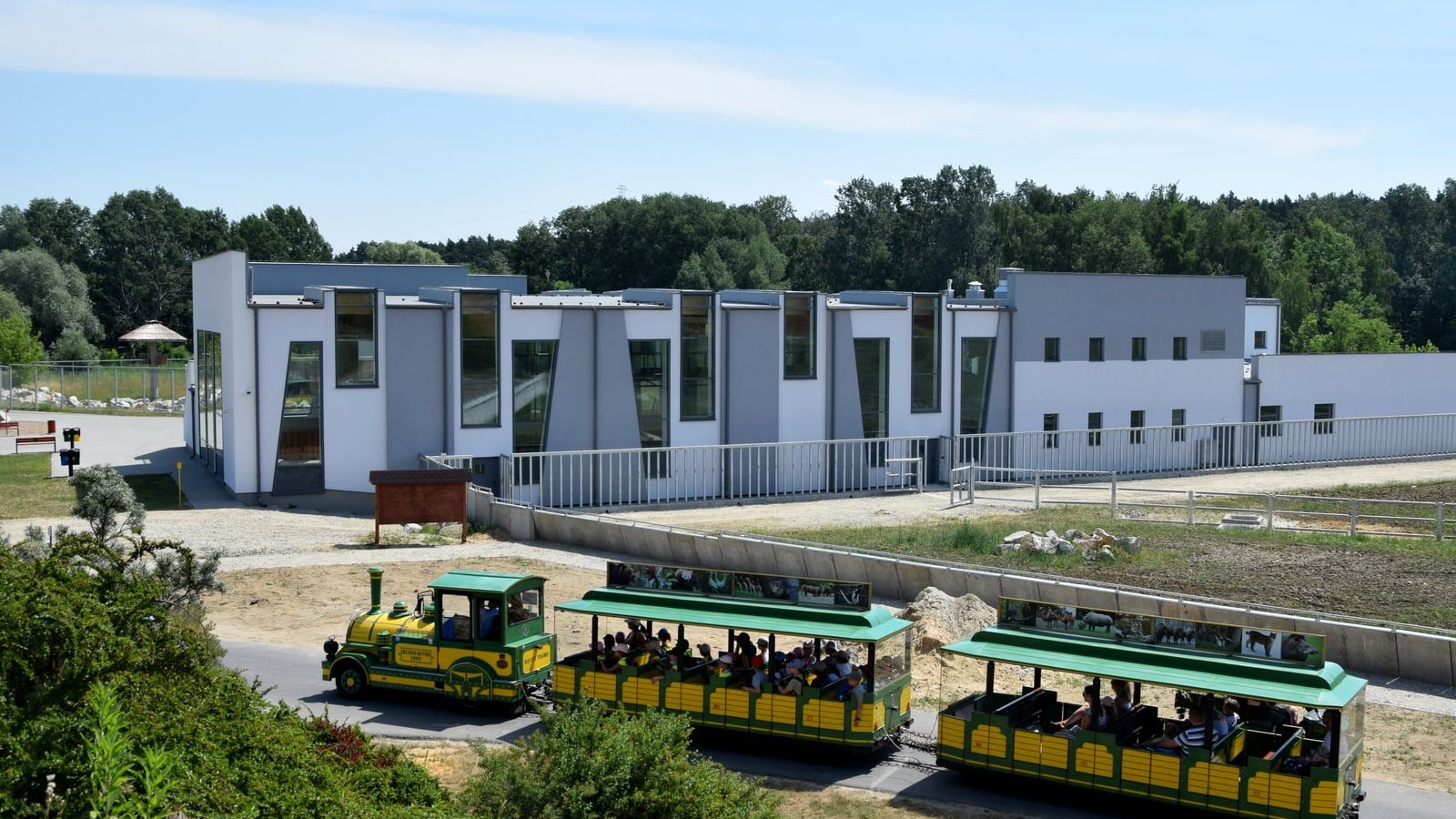 Zdjęcie przedstawia kolejkę jadącą przez teren zoo. W tle widać nowy pawilon żyraf.