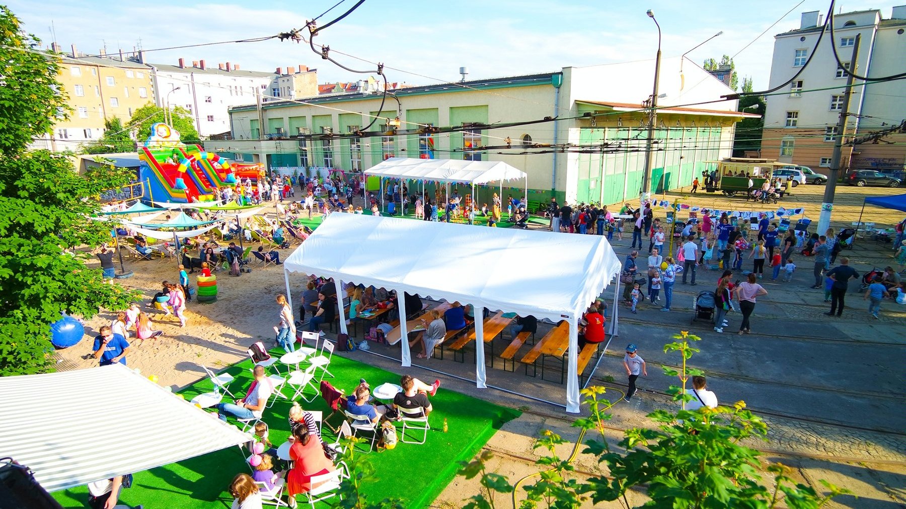 Zdjęcie przedstawia tłum ludzi w dawnej zajezdni tramwajowej. Widać na na nim m.in. białe namioty, dmuchaną zjeżdżalnię, plażę czy stoliki z krzesłami.