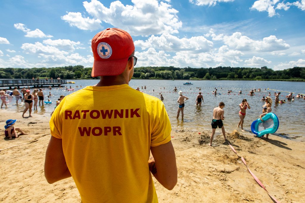 Ratownik nad jeziorem. W tle jezioro i kąpiący się ludzie. - grafika rozmowy