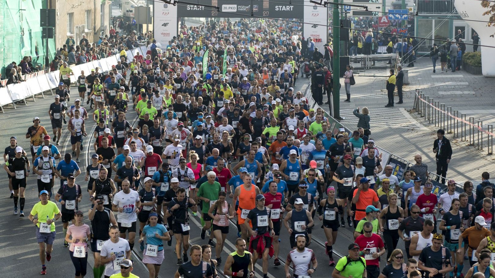 Zdjęcie przedstawia biegaczy podczas Poznańskiego Maratonu. Tłum ludzi biegnie ulicami Poznania.