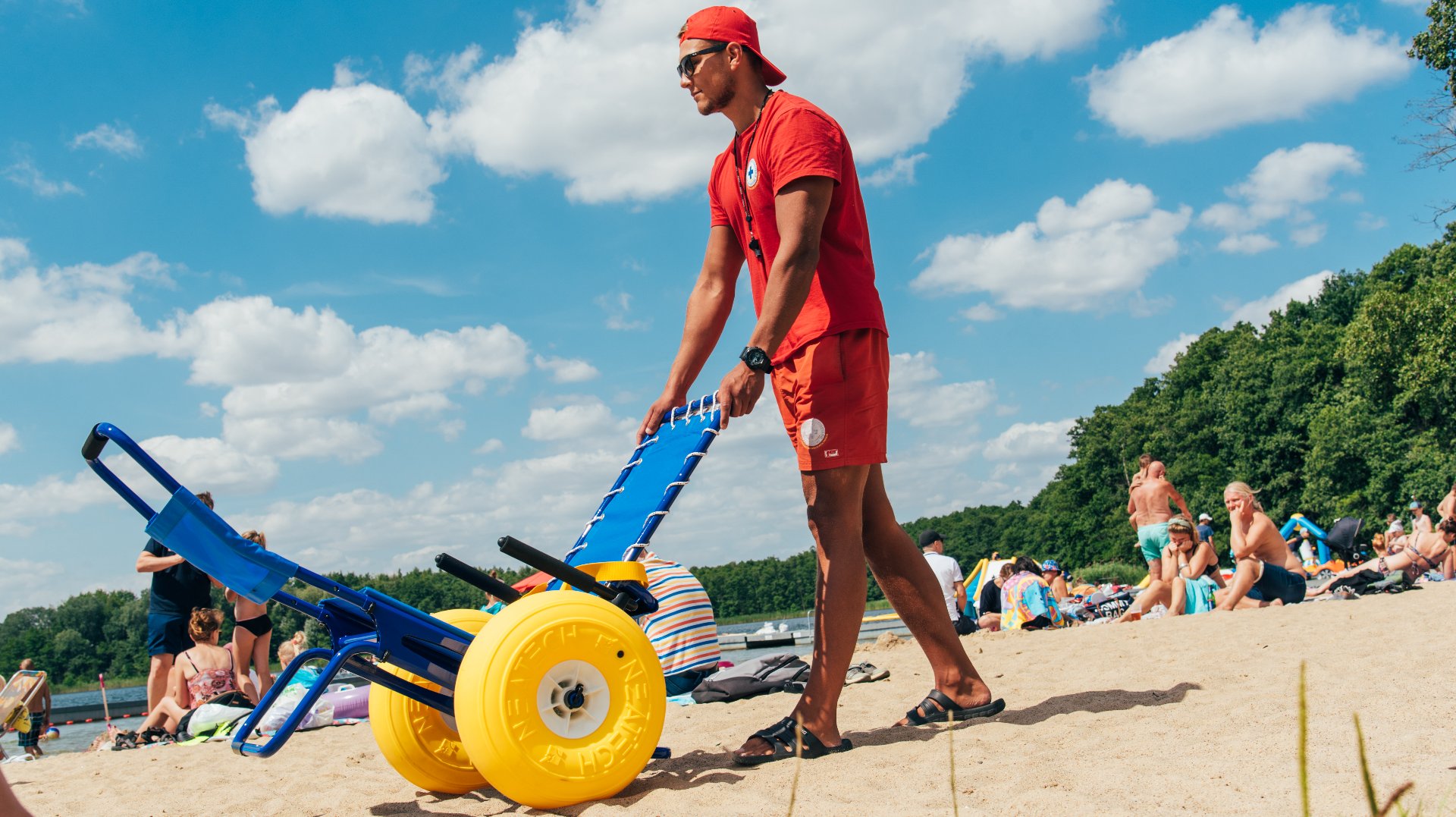 Zdjęcie przedstawia ratownika z wózkiem na plaży. Pcha on przed sobą wózek amfibie. - grafika rozmowy