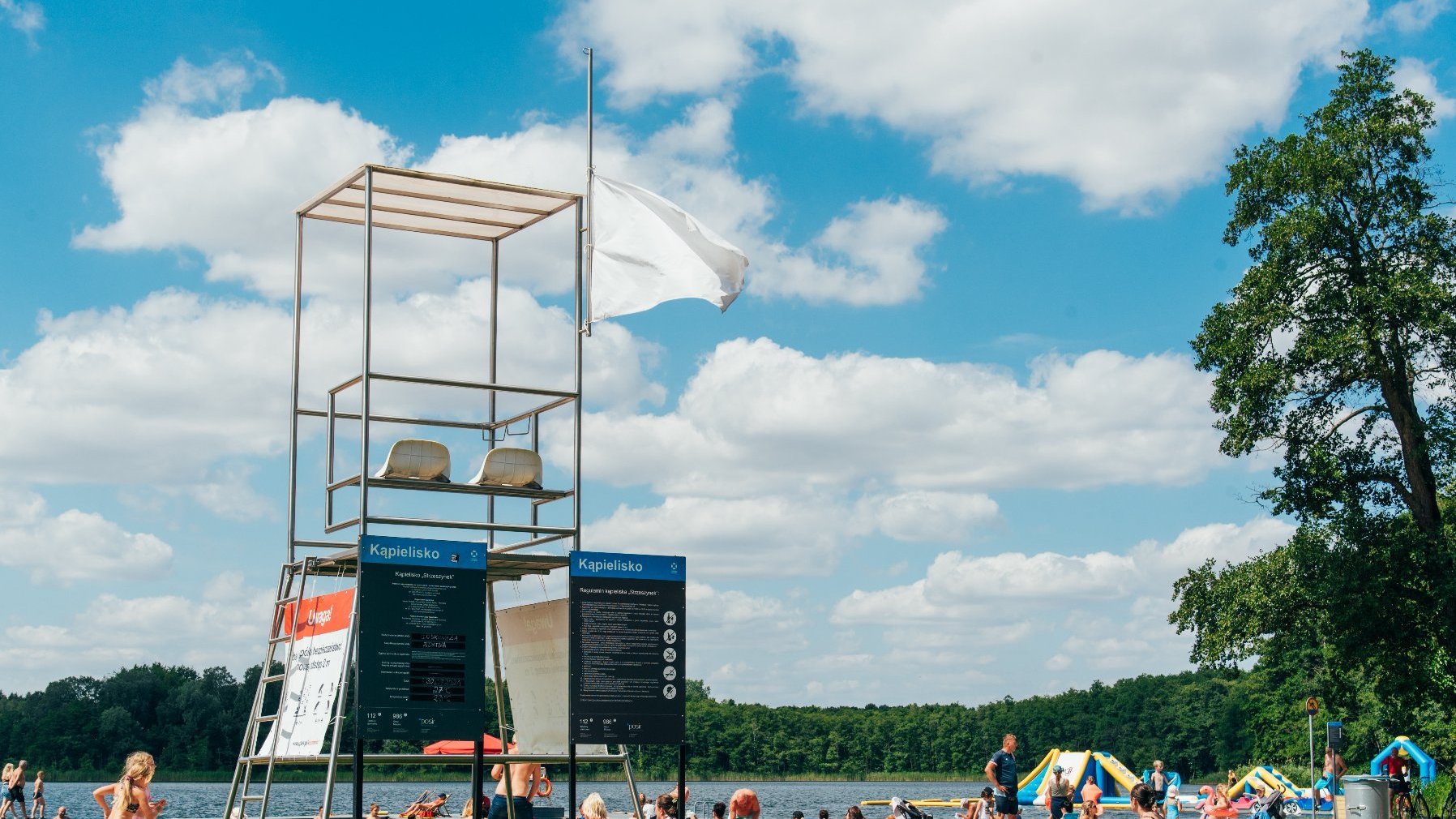 Zdjęcie przedstawia plażę, na której siedzą ludzie. Widać na nim także podest ratownika.