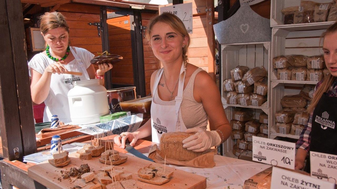 Zdjęcie przedstawia kobietę przy stoisku z chlebem.