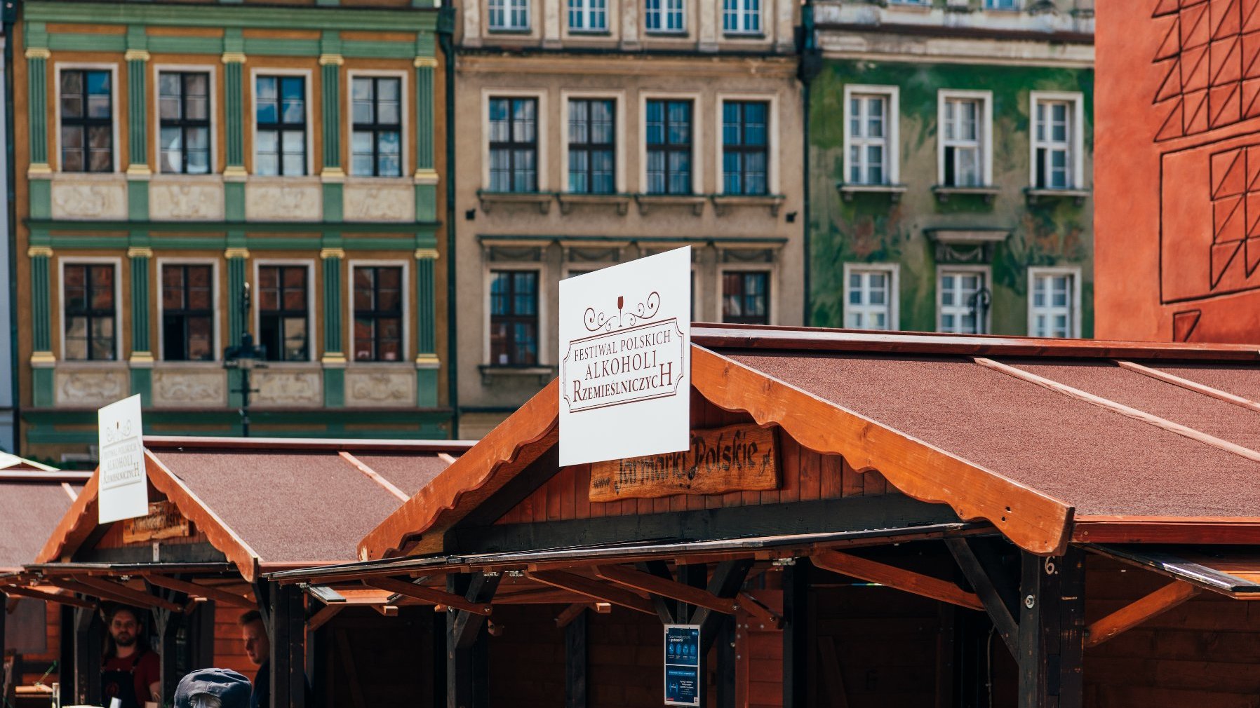 Zdjęcie przedstawia drewniane domki, na których znajduje się logo z napisem "Festiwal Polskich Alkoholi Rzemieślniczych".