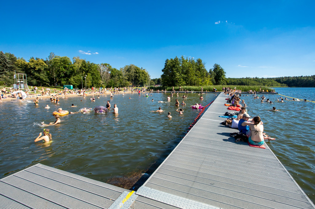 Zdjęcie przedstawia kąpielisko. Widać na nim pomost i wodę, w oddali także plażę. Wszędzie jest tłum ludzi. - grafika rozmowy