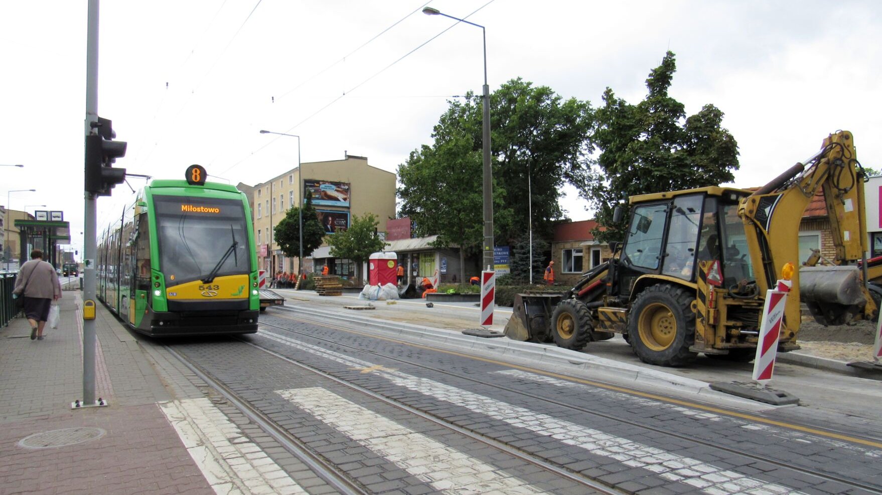 Dwa przystanki tramwajowe. Przy jednym stoi tramwaj, drugi przebudowywany jest na wiedeński, widać płyty i koparkę