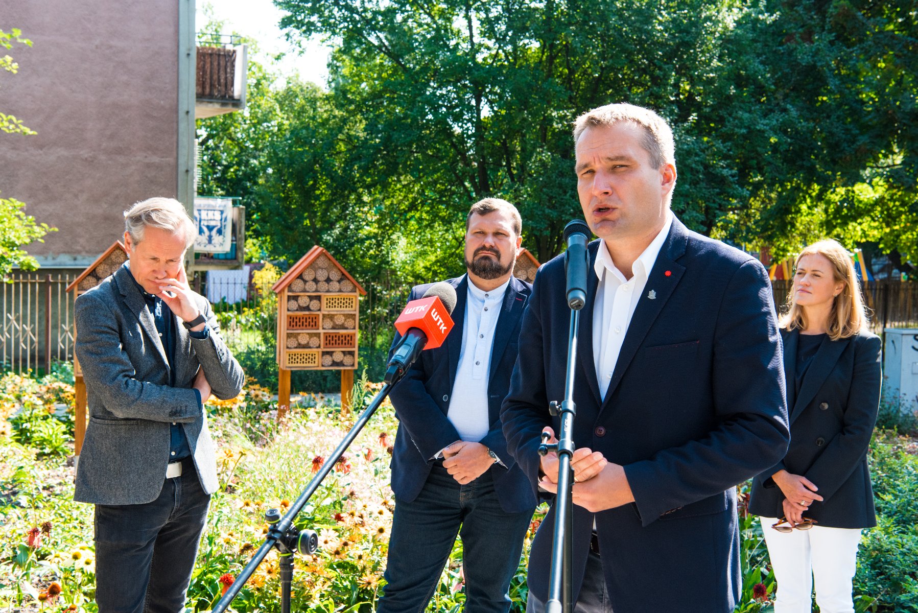 Galeria zdjęć przedstawia konferencję prasową na skwerze oraz sam skwer z zielenią i domkami dla owadów. - grafika rozmowy