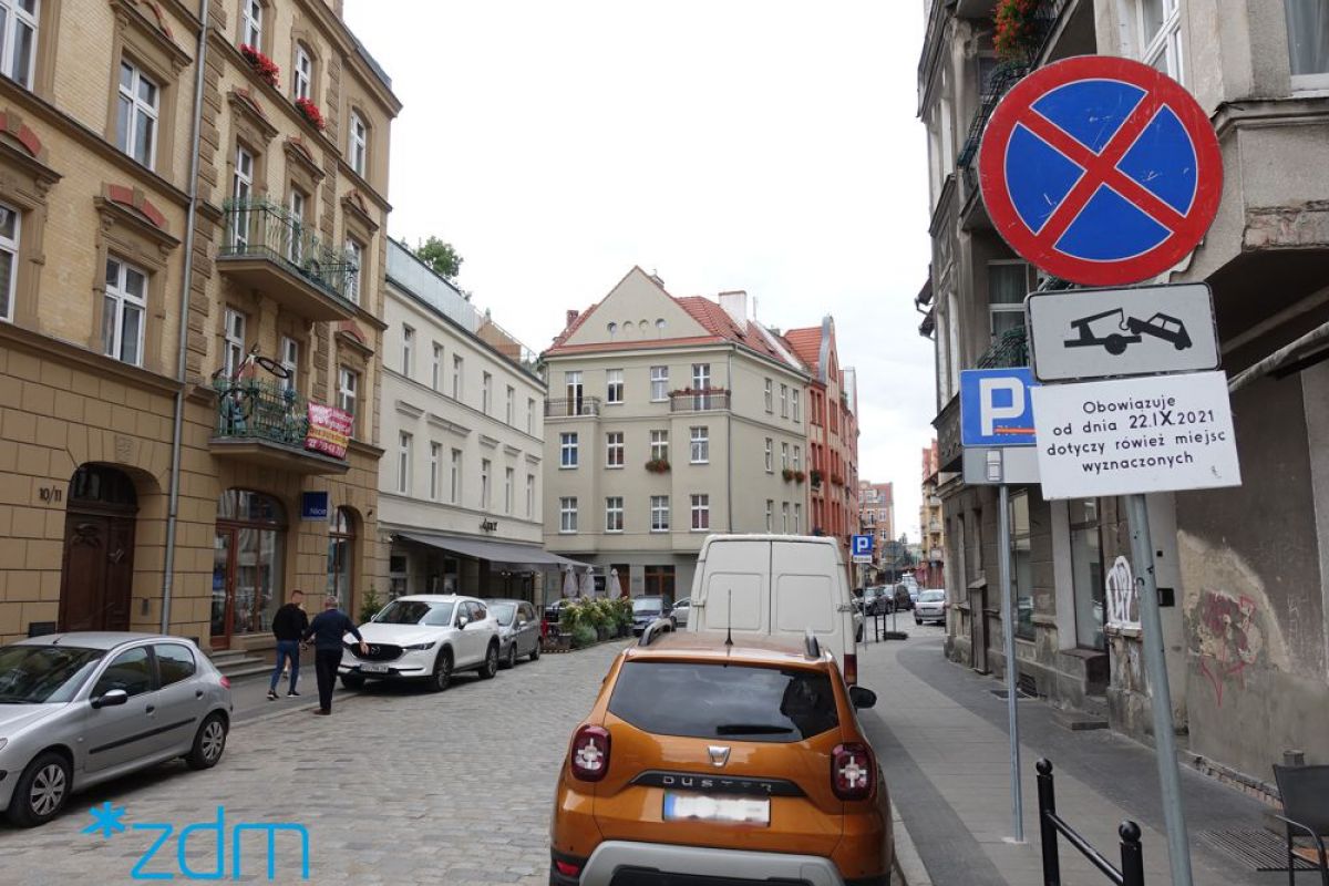 Zdjęcie pokazuje ulicę na Śródce, gdzie postawiono oznakowanie informujące o zmianie organizacji ruchu i konieczności przeparkowania aut na czas prac - grafika rozmowy