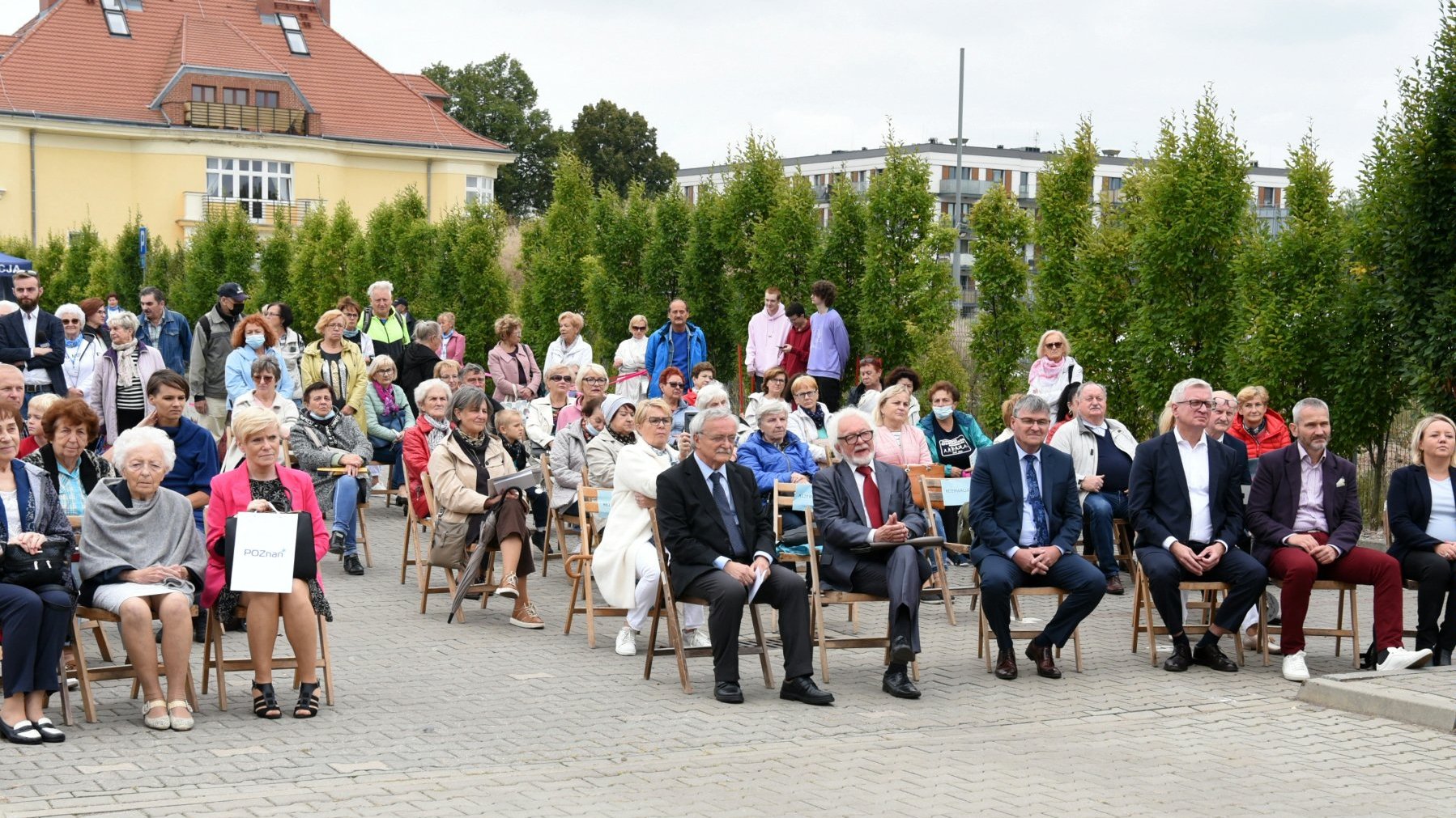 Seniorzy siedzący na krzesłach, patrzący w stronę sceny, wśród nich Jacek Jaśkowiak i Jędrzej Solarski - prezydent miasta i jego zastępca