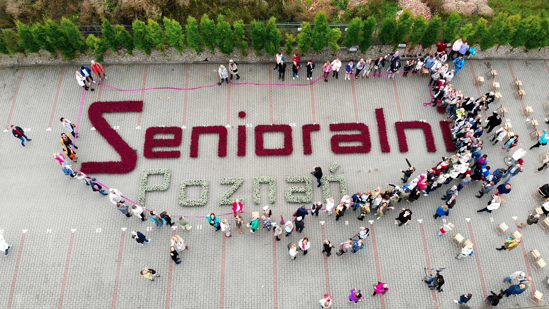 zdjęcie z lotu ptaka, napis: Senioralni Poznań ułożony z kwiatów, wokół zgromadzeni ludzie