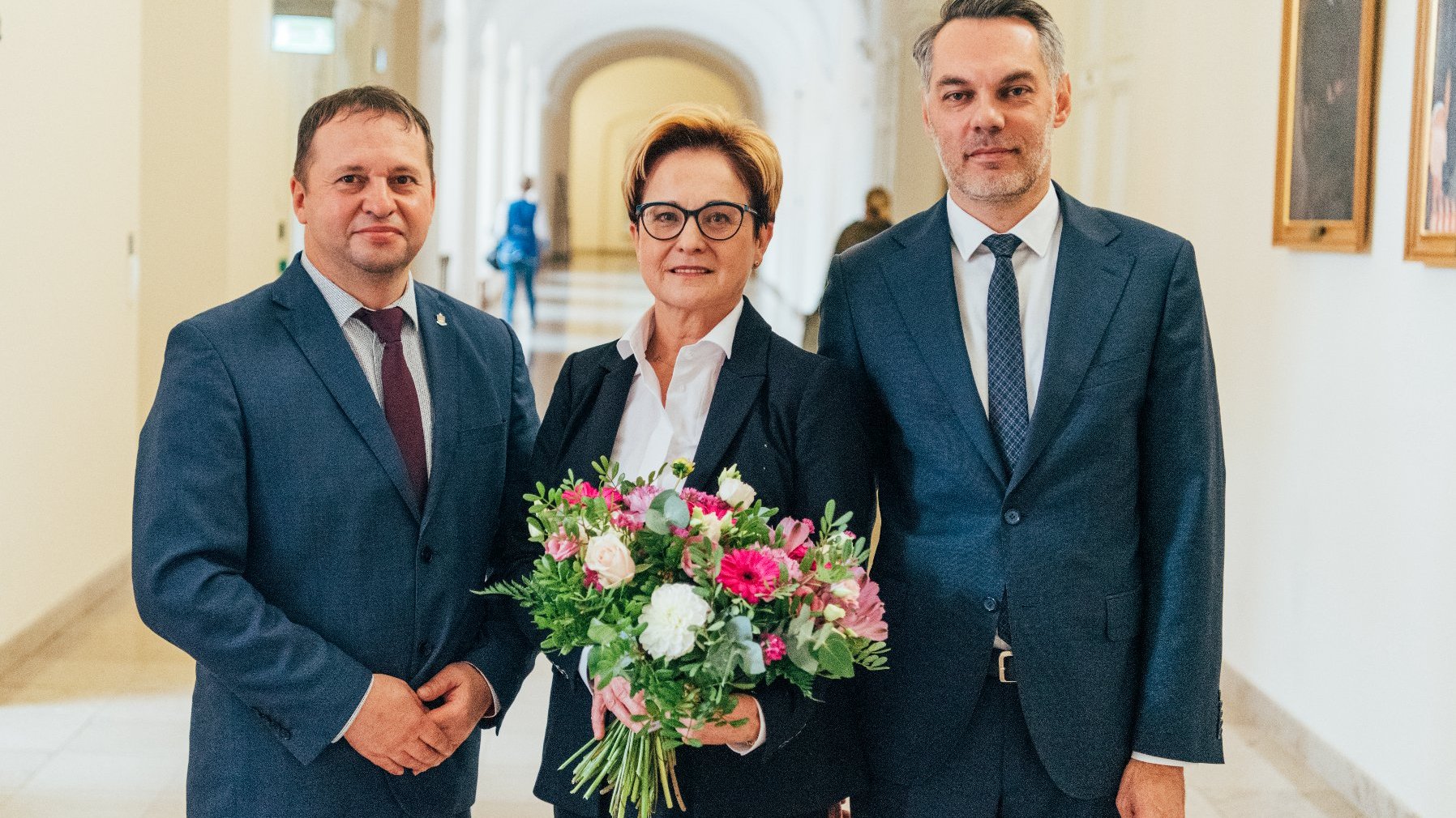 Trzy osoby stoją w rzędzie, w centrum Barbara Sajnaj z kwiatami w ręku, obok Piotr Husejko, nowy skarbnik oraz Wojciech Kasprzak, dyrektor Wydziału Organizacyjnego UMP