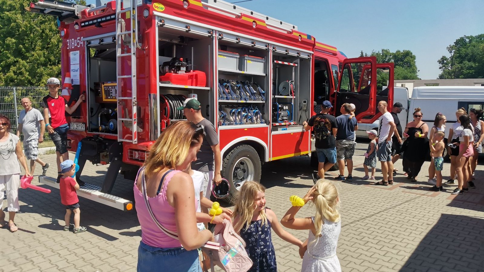 Zdjęcie przedstawia ludzi oglądających wóz strażacki.