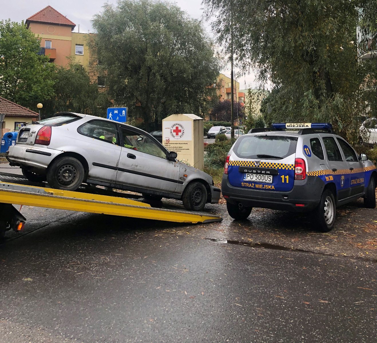 Zdjęcie przedstawia holowany samochód wciągany na lawetę. Obok znajduje się auto straży miejskiej. - grafika rozmowy