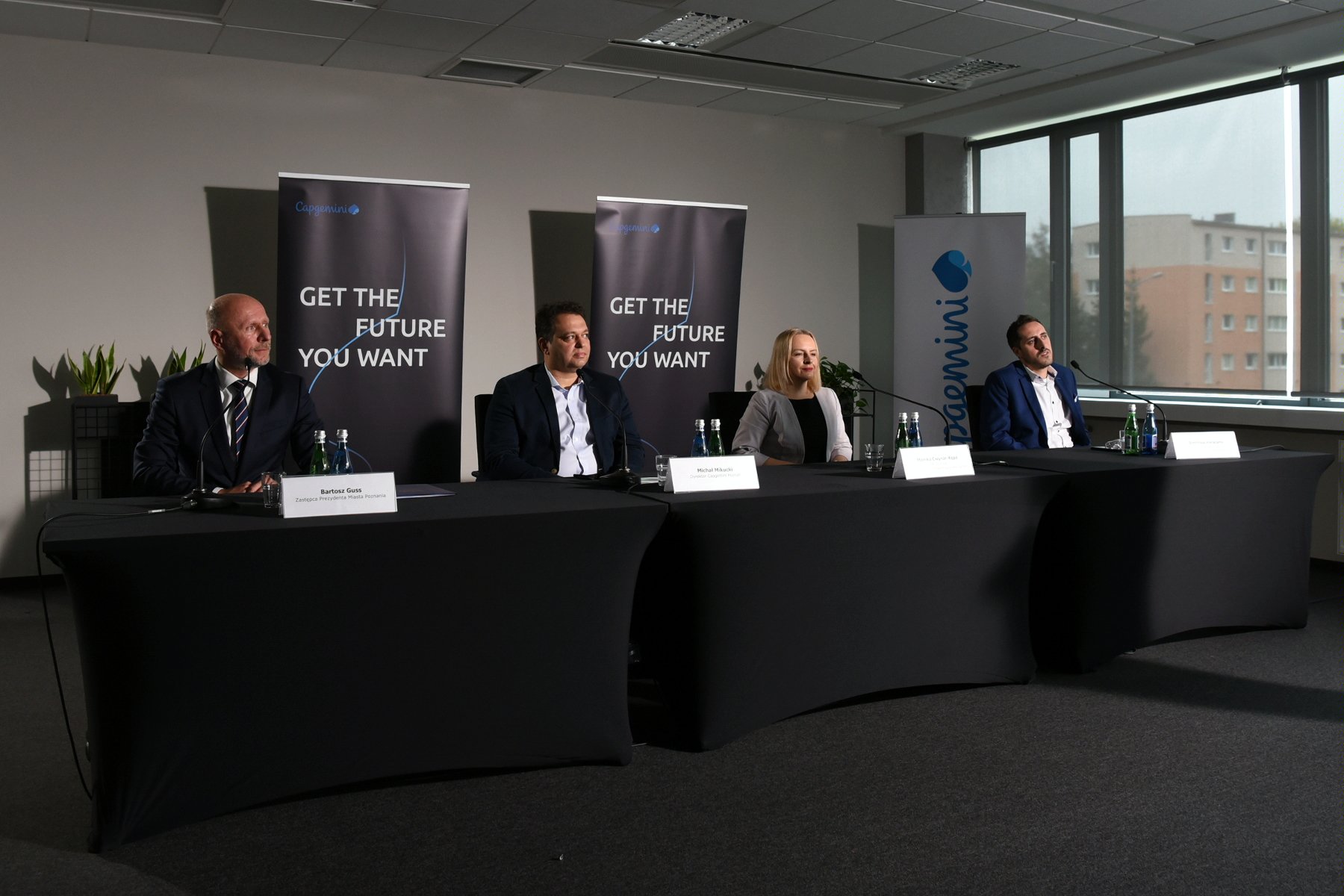 Zdjęcie przedstwia cztery osoby siedzące za stołem konferencyjnym podczas briefingu prasowego. - grafika rozmowy