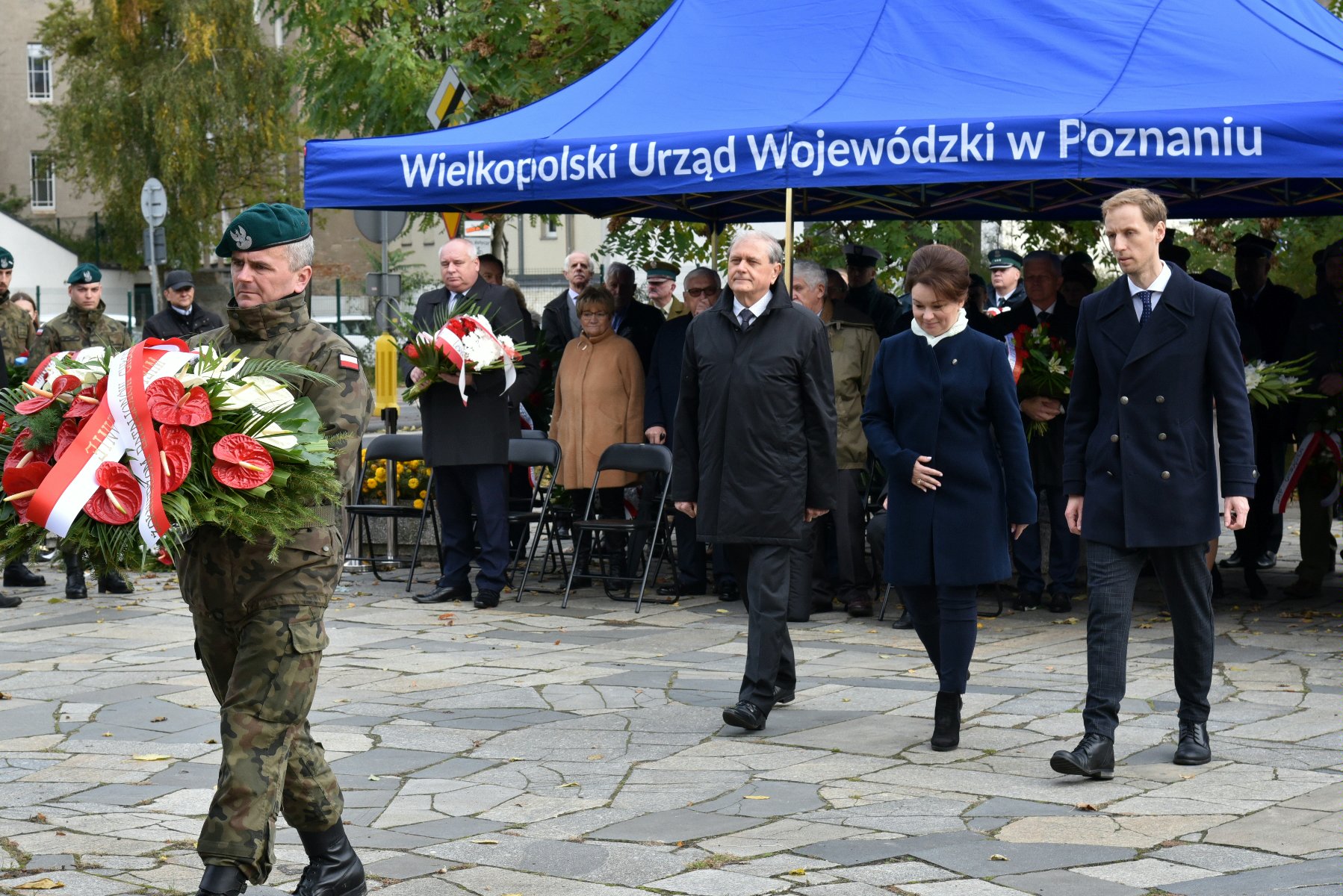 Na zdjęciu przedstawiciele władz miasta i województwa obok siebie, przed nimi żołnierz trzymający wiązankę kwiatów - grafika rozmowy