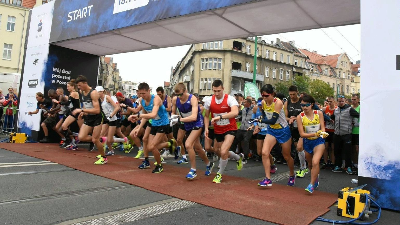 Na zdjęciu start poznańskiego biegu, na starcie dziesiątki biegaczy, którzy właśnie rozpoczynają bieg - grafika rozmowy