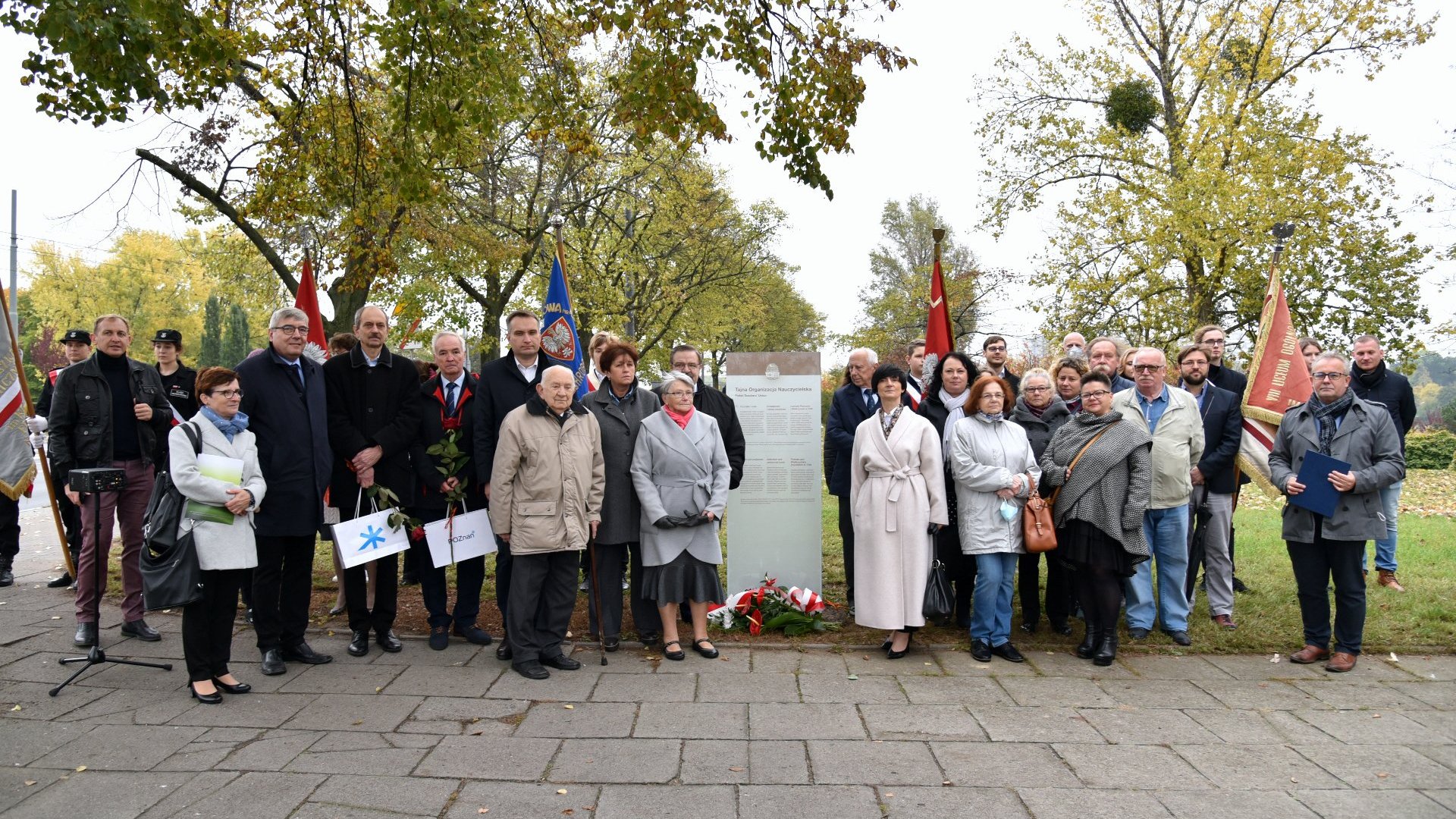 Zdjęcie przedstawia uczestników uroczystości na zdjęciu grupowym przy tablicy.