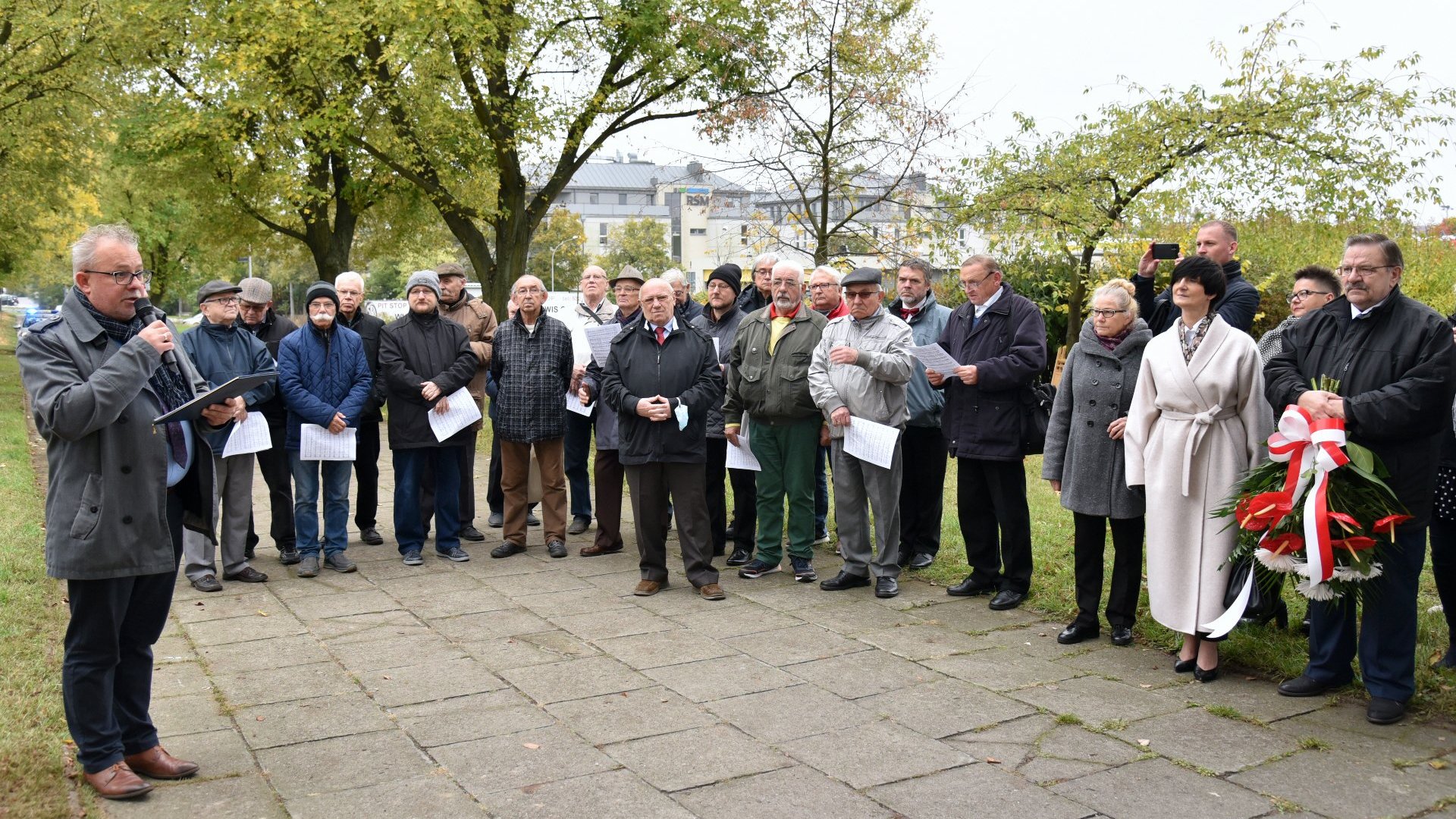 Zdjęcie przedstawia tłum zgromadzony przed tablicą.