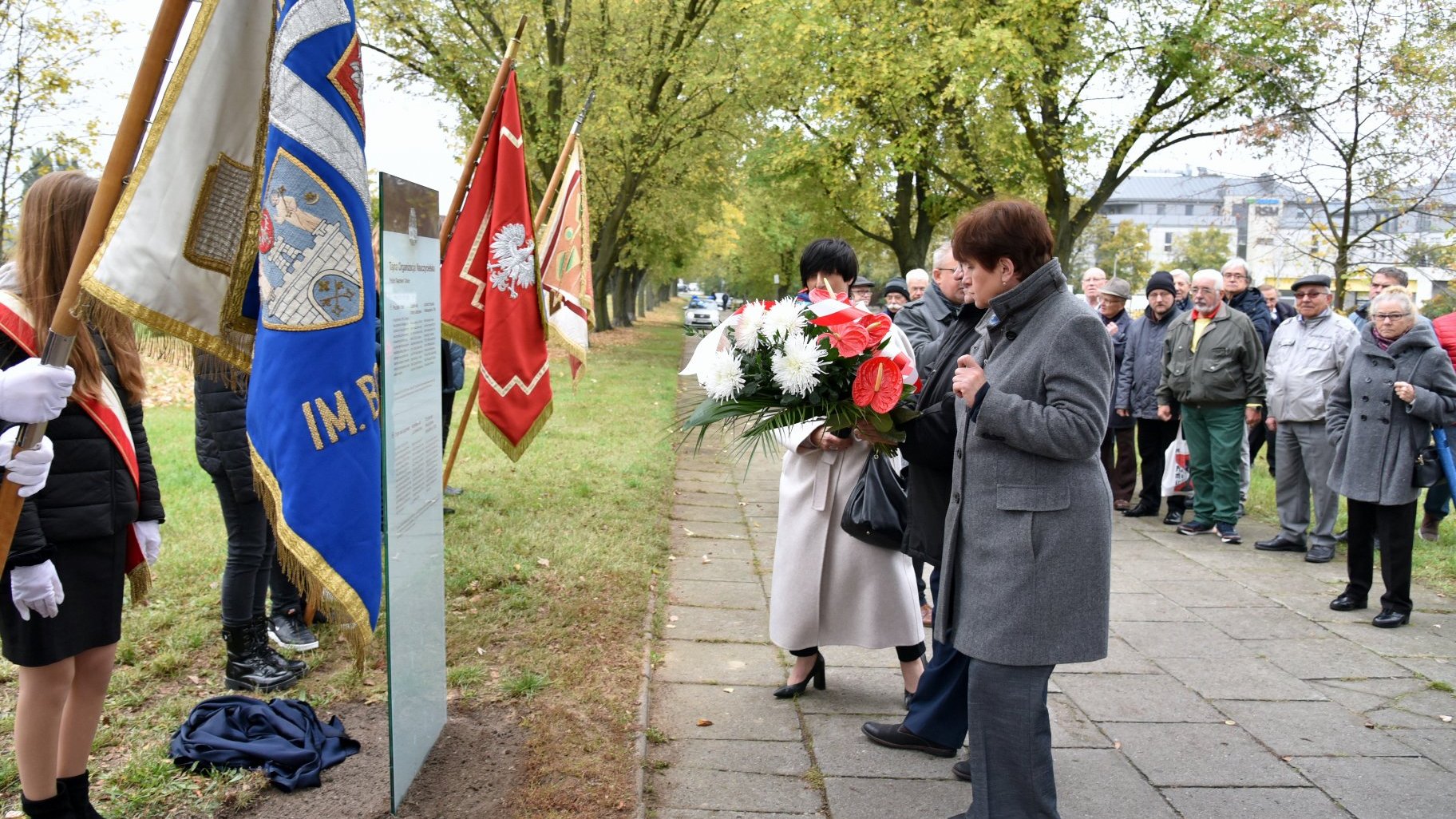 Zdjęcie przedstawia przedstawiciele ZNP składających kwiaty pod tablicą.