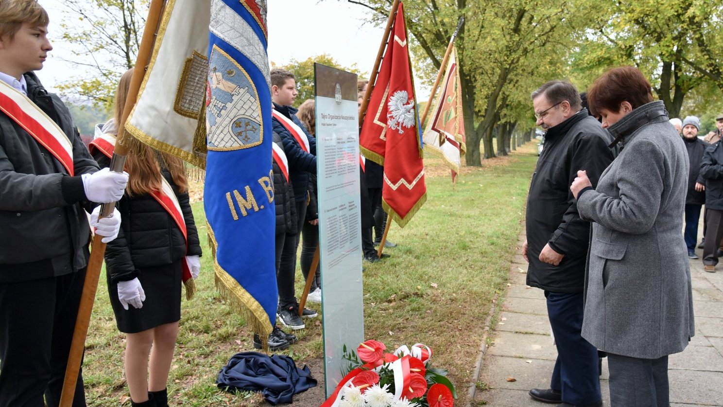 Zdjęcie przedstawia przedstawiciele ZNP składających kwiaty pod tablicą.