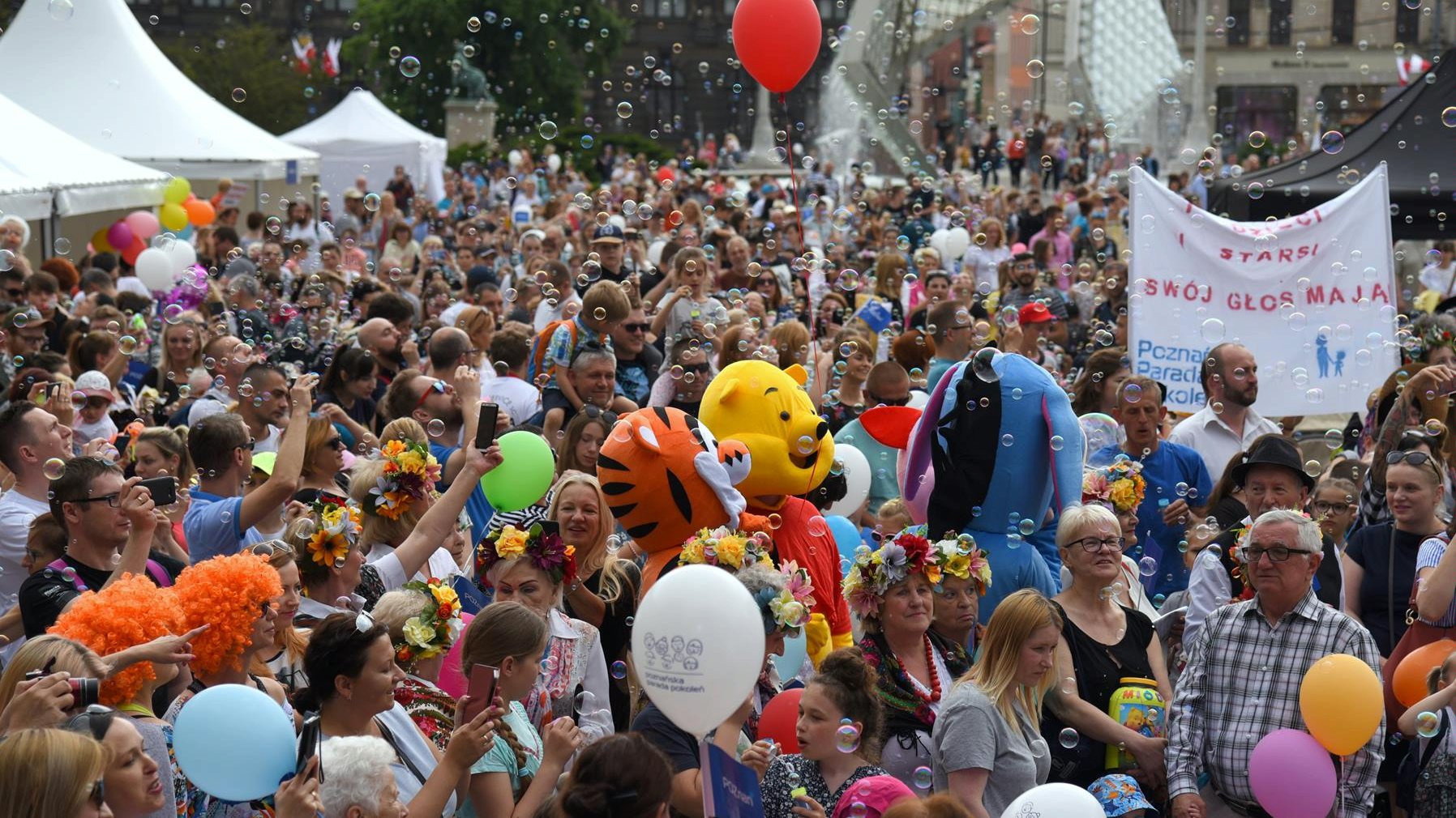 Na zdjęciu Parada Pokoleń, która kończyła Poznańskie Dni Rodziny 2019 - widać dużo uśmiechniętych ludzi, niosą balony, puszczają bańki mydlane - grafika rozmowy