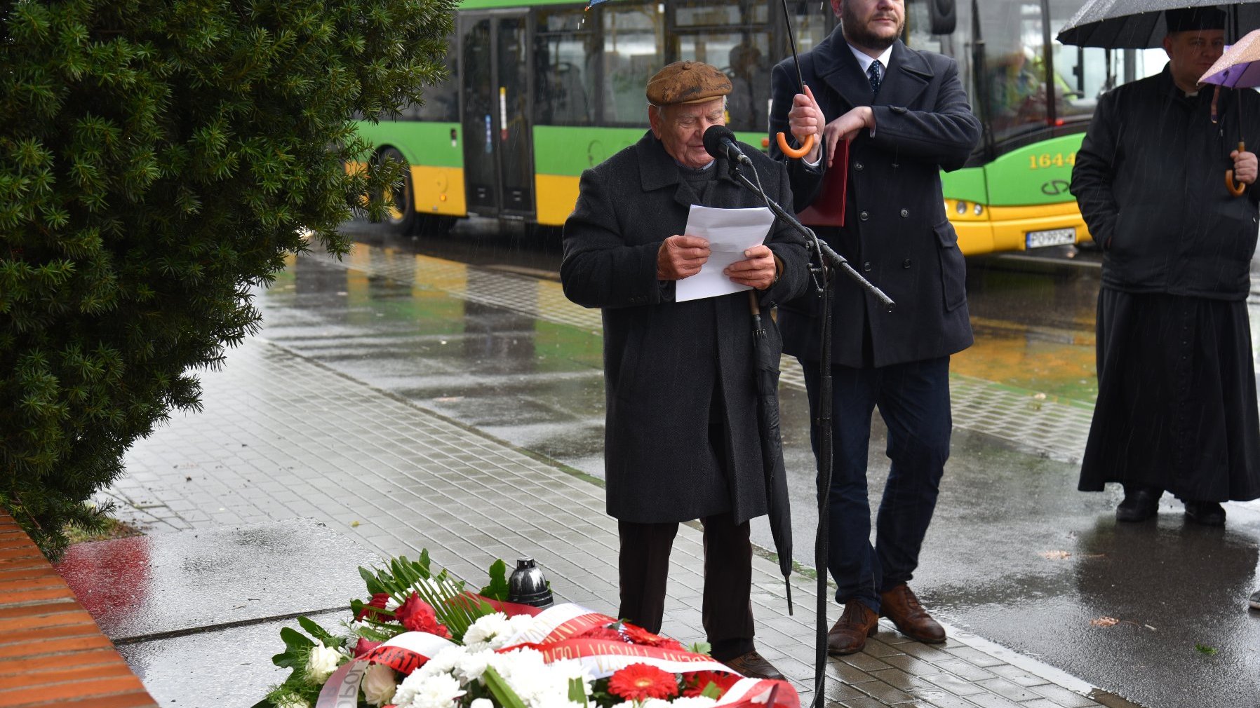 Zdjęcie przedstawia przemawiającego do mikrofonu mężczyznę.