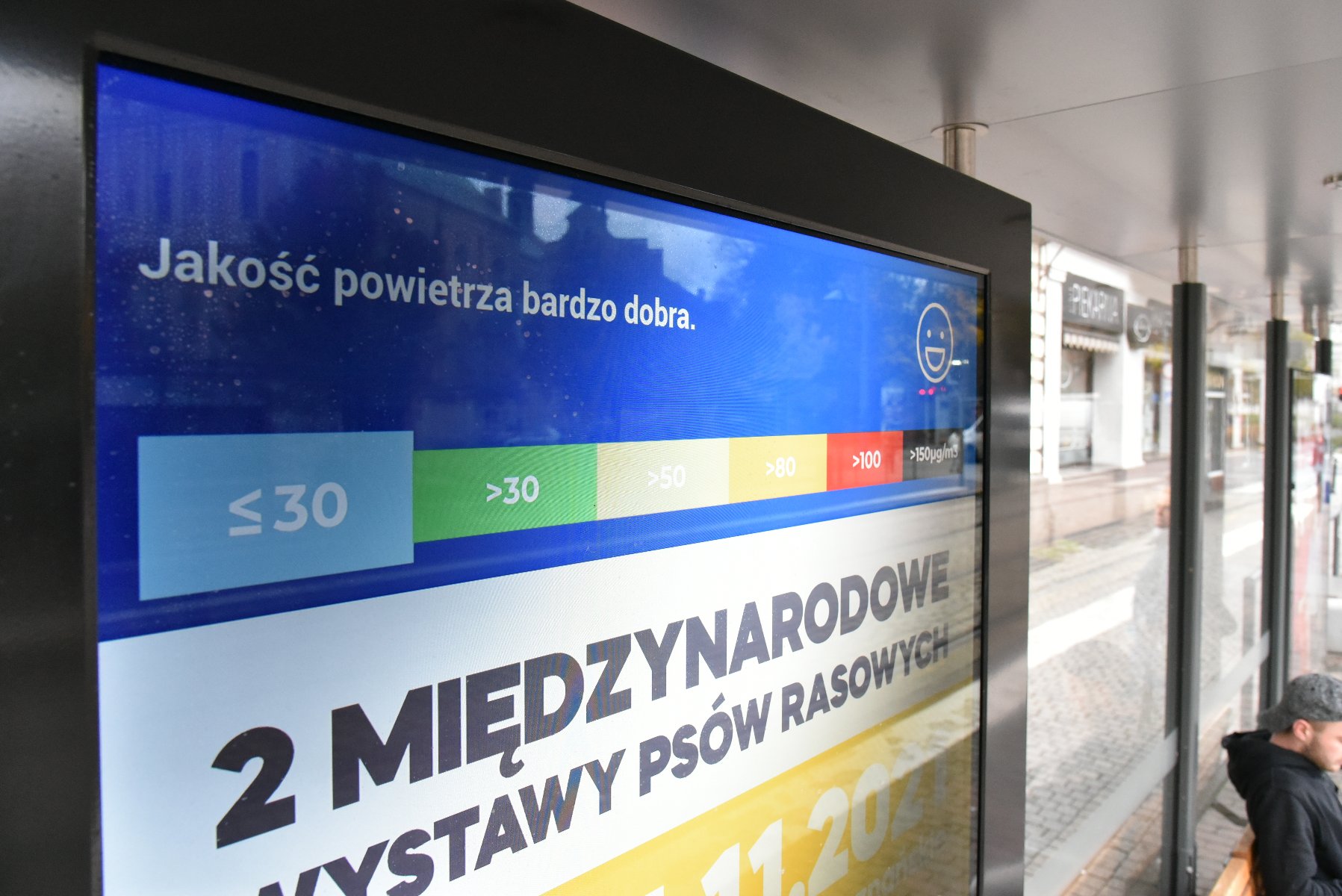 Galeria zdjęć przedstawia ekran z reklamą i informacją o jakości powietrza, znajdujący się na przystanku komunikacji miejskiej. - grafika rozmowy