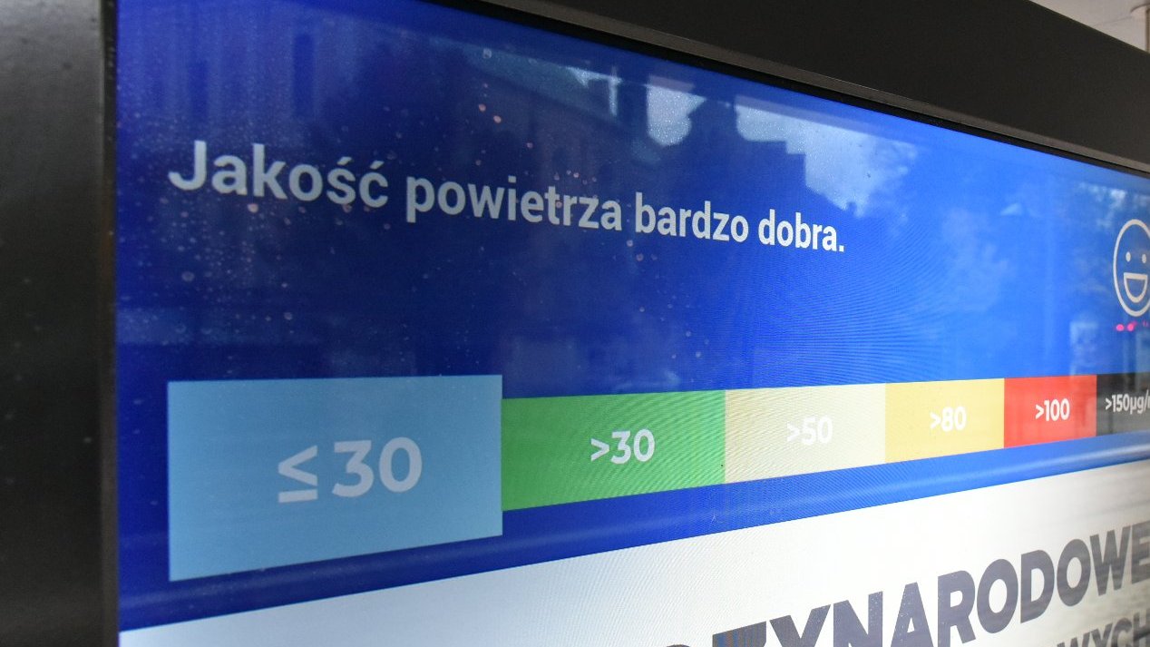 Galeria zdjęć przedstawia ekran z reklamą i informacją o jakości powietrza, znajdujący się na przystanku komunikacji miejskiej.