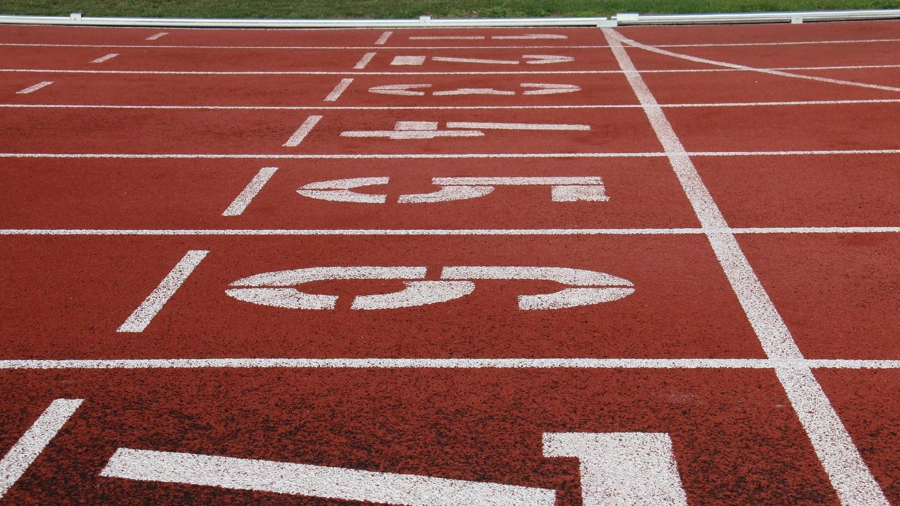 Bieżnia lekkoatletyczna z widocznymi numerami startowymi. - grafika rozmowy