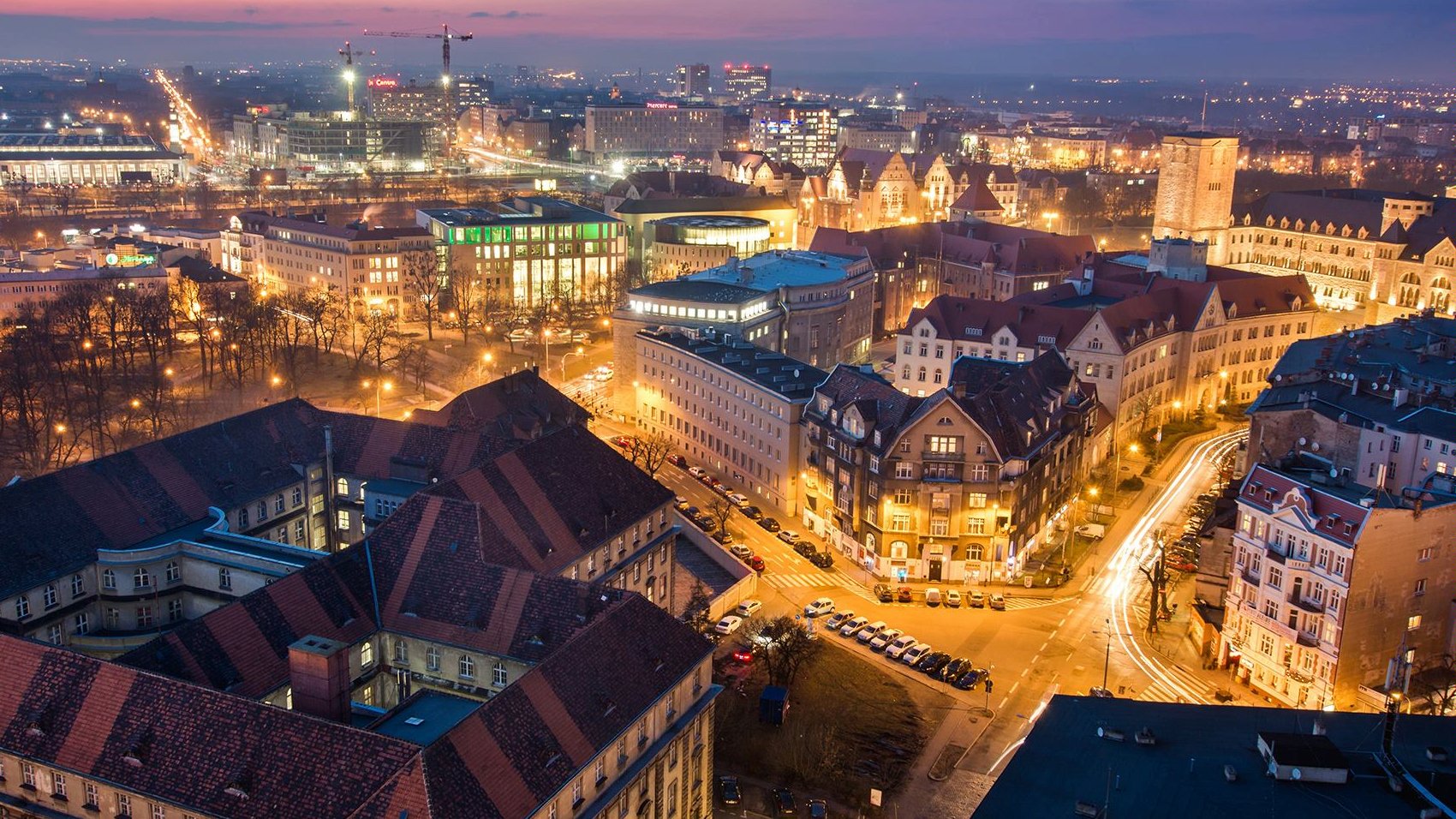 Na zdjęciu panorama Poznania po zmroku, w centrum dachy kamienic - grafika rozmowy