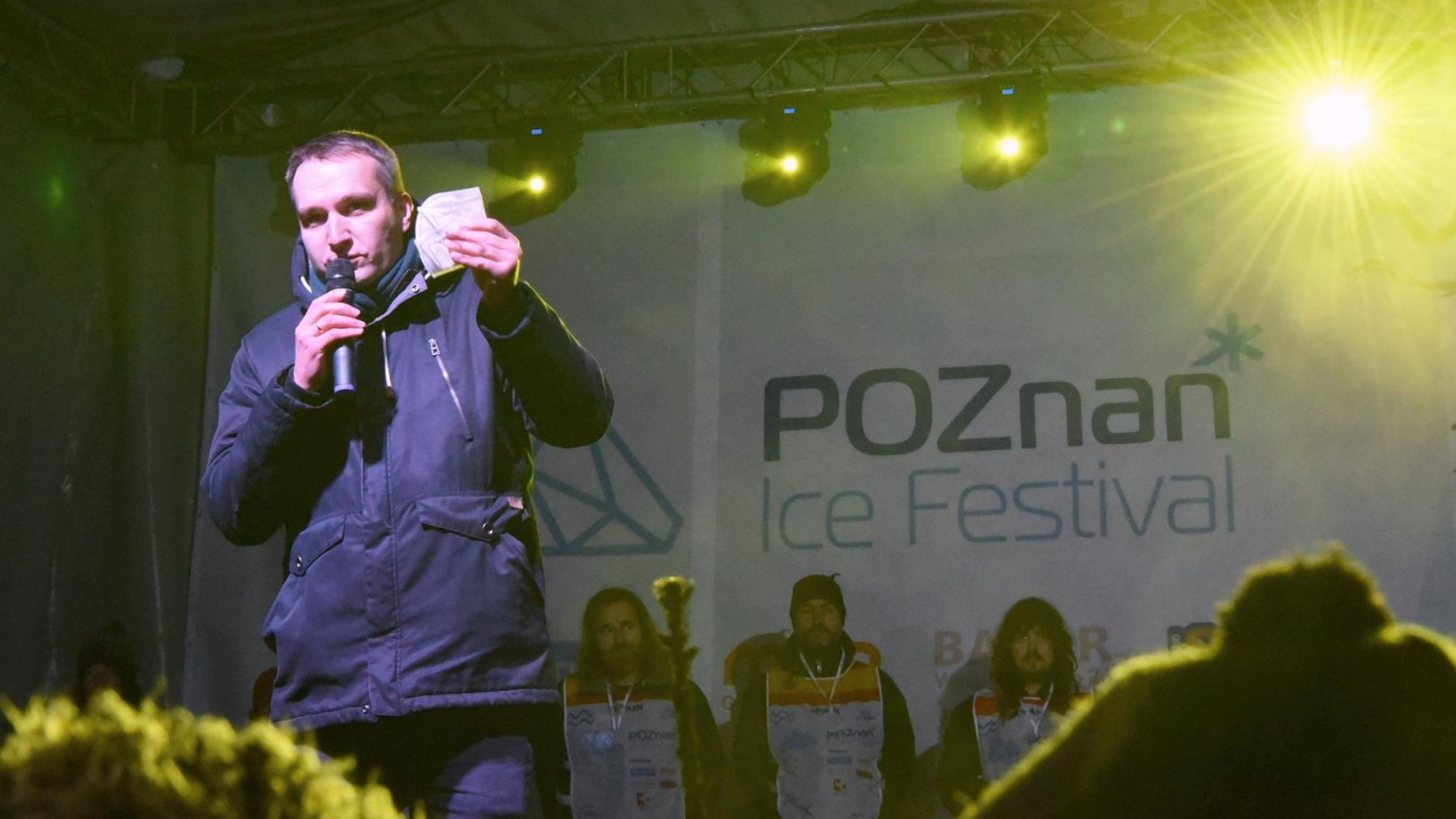 Na zdjęciu Mariusz Wiśniewski, zastępca prezydenta Poznania, na scenie, z maseczką w ręku, apelujący o zachowanie zasad bezpieczeństwa