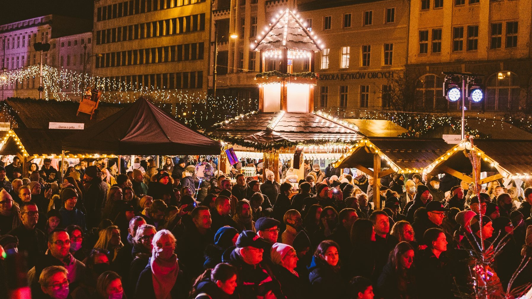 Galeria zdjęć przedstawia jarmark na placu Wolności. Widać na nim drewniane domki handlowe i tłum ludzi.