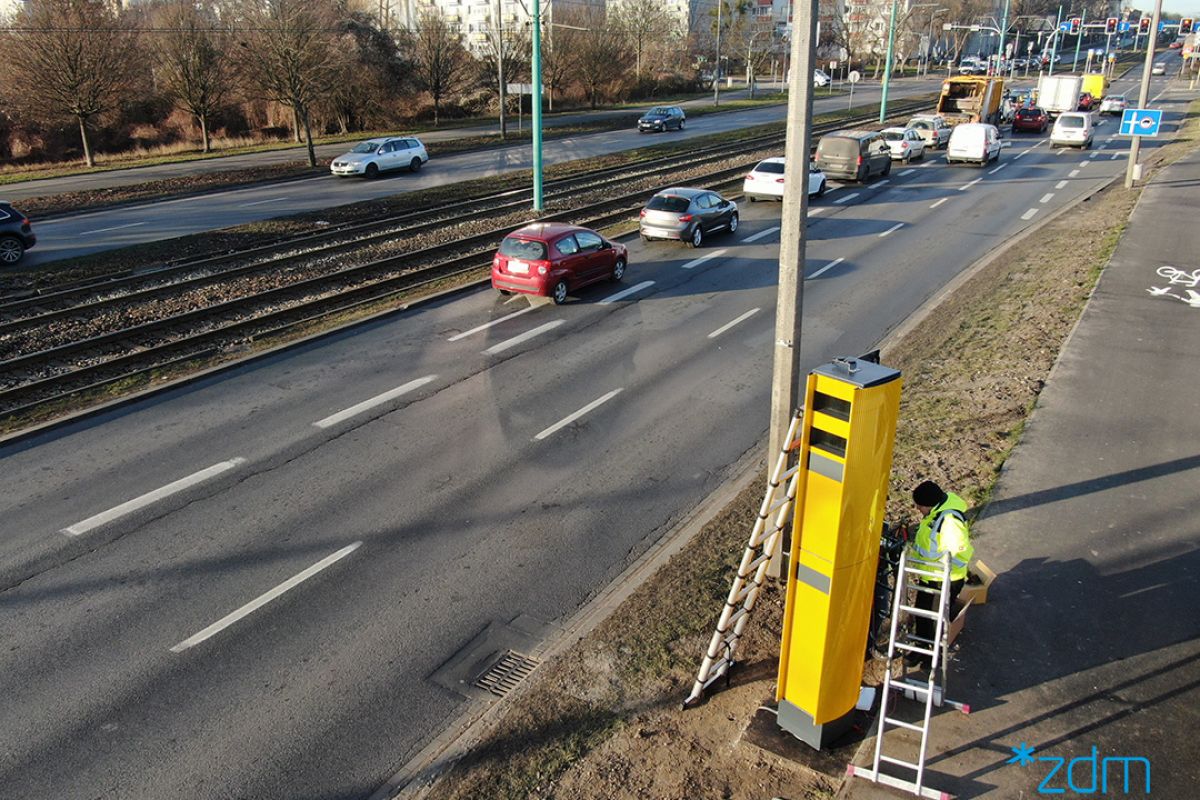 Sznur samochodów na ul. Hetmańskiej. Na poboczu trwa montaż fotoradaru. - grafika rozmowy