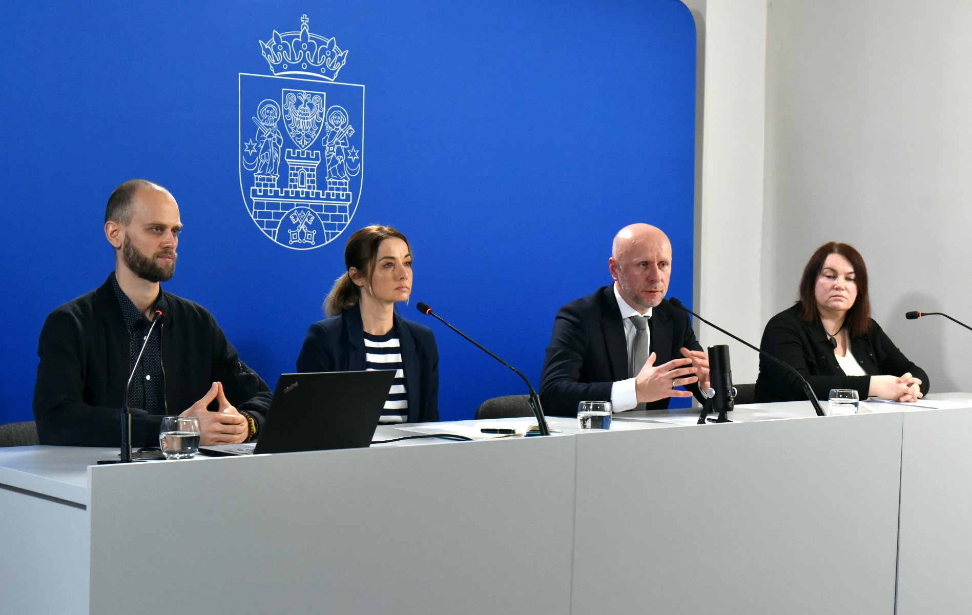 Galeria zdjęć przedstawia zdjęcia z konferencji prasowej. Widać na nich ludzi siedzących za stołem konferencyjnym. - grafika rozmowy