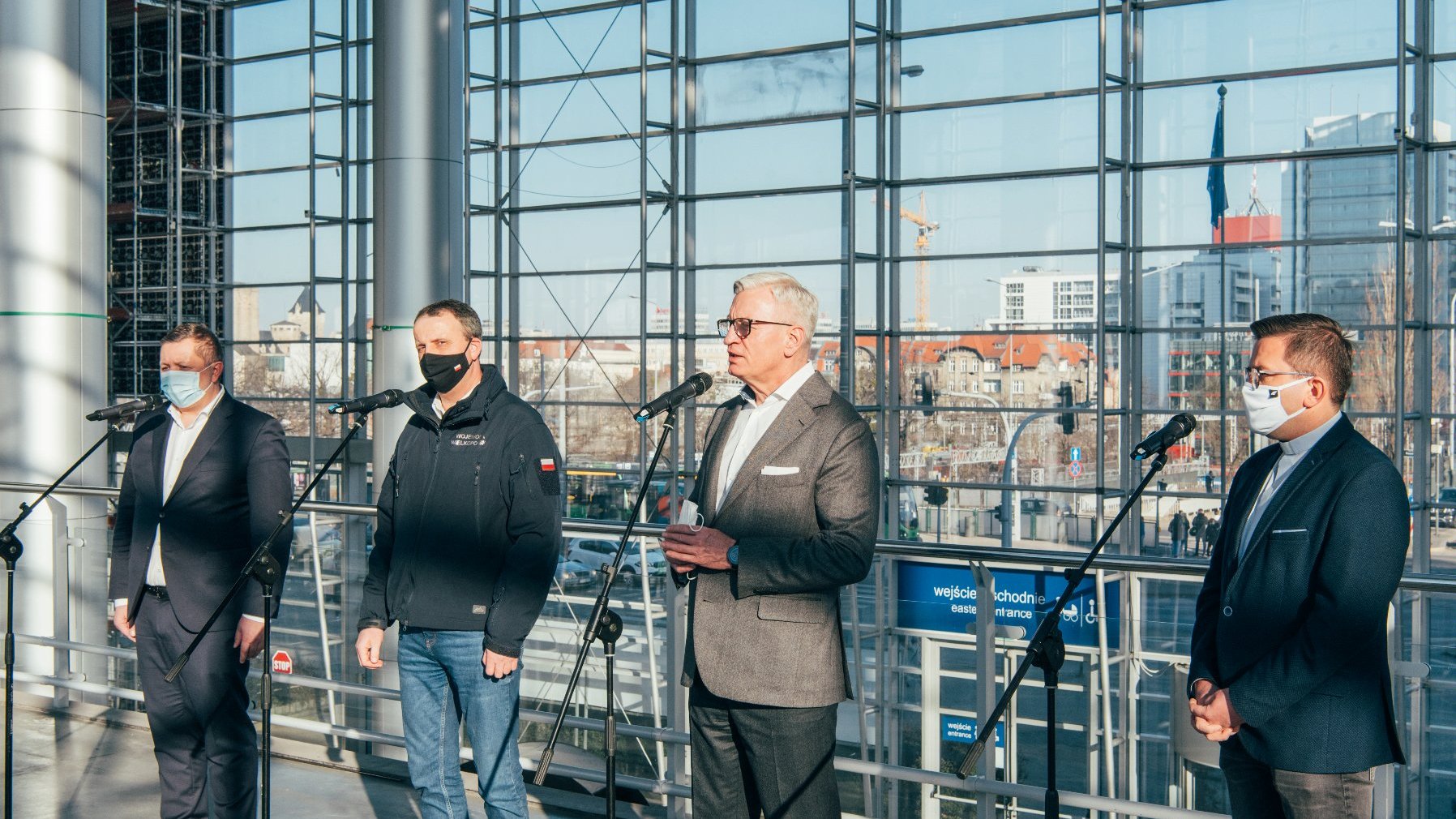 Czterej mężczyźni przed mikrofonami: prezydent Poznania, wojewoda wielkopolski, prezes Grupy MTP i dyrektor Caritas