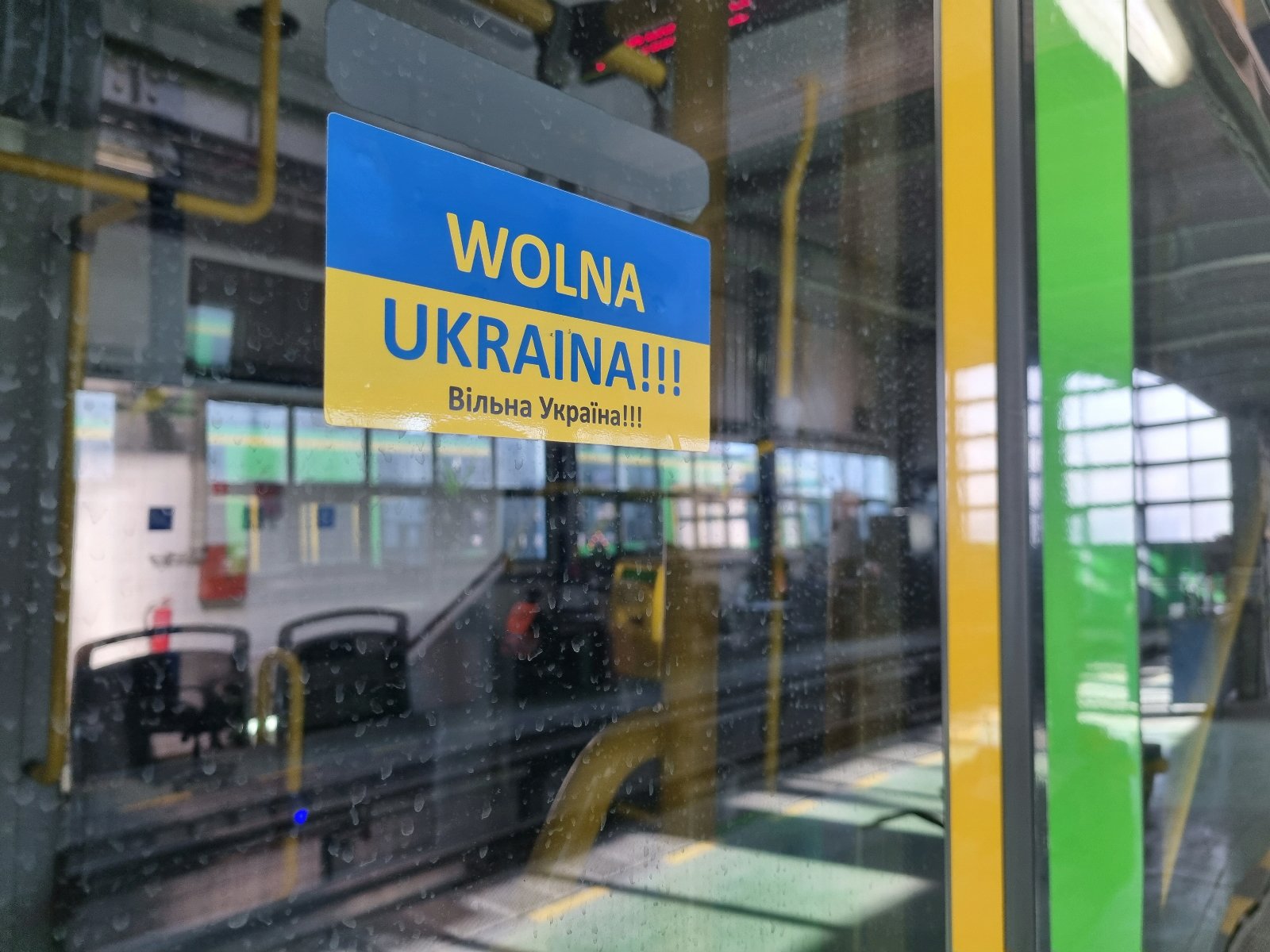 Niebiesko-żółta naklejka z napisem Wolna Ukraina po polsku i ukraińsku naklejona na drzwiach tramwaju - grafika rozmowy