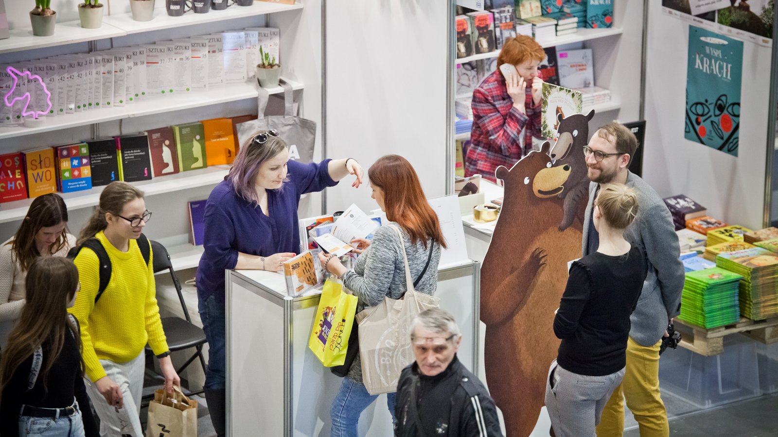 Galeria zdjęć przedstawia stoiska z książkami we wnętrzu hali targowej oraz oglądających je ludzi.