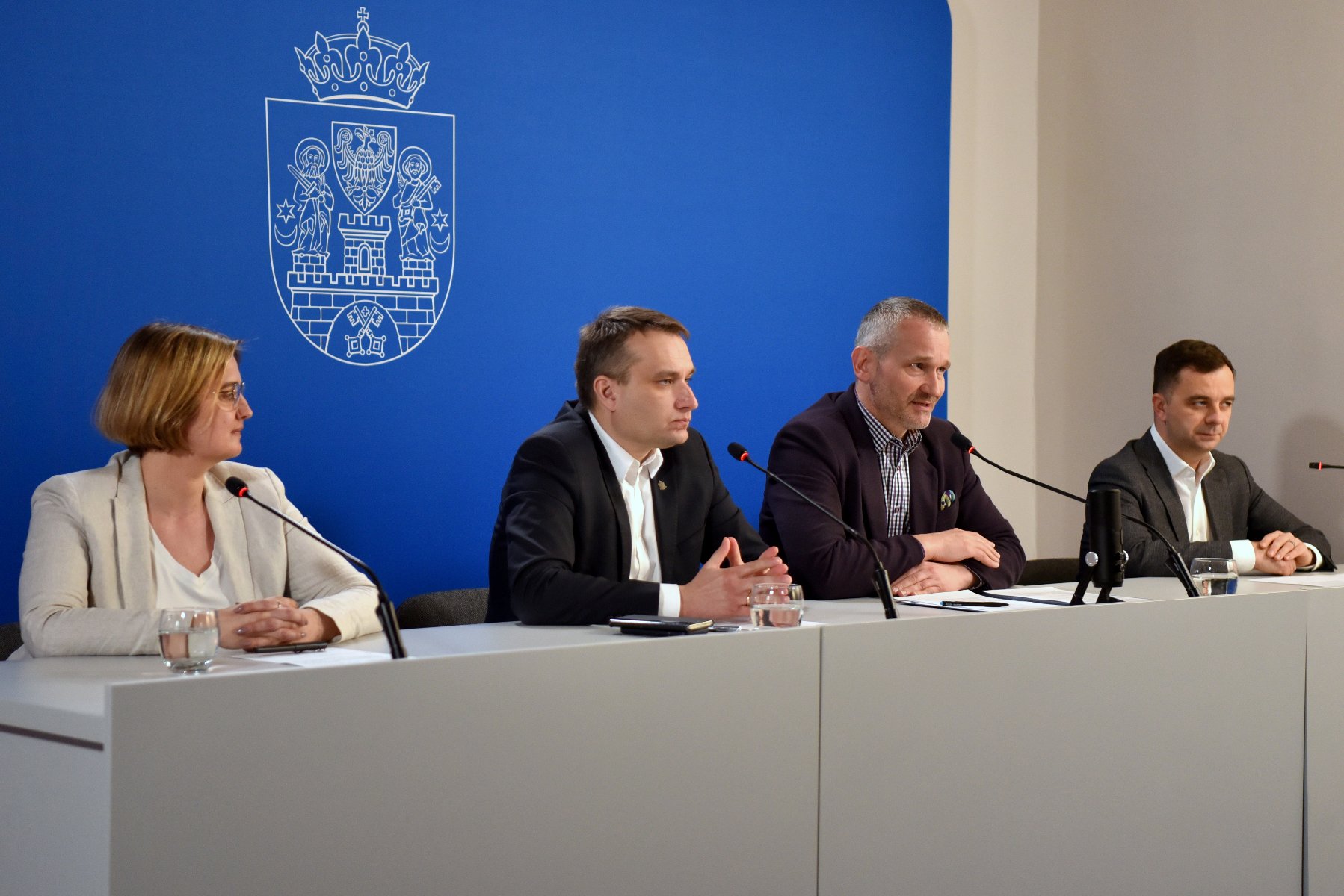 Na zdjęciu cztery osoby za stołem konferencyjnym, w środku dwaj zastępcy prezydenta Poznania: Mariusz Wiśniewski i Jędrzej Solarski - grafika rozmowy