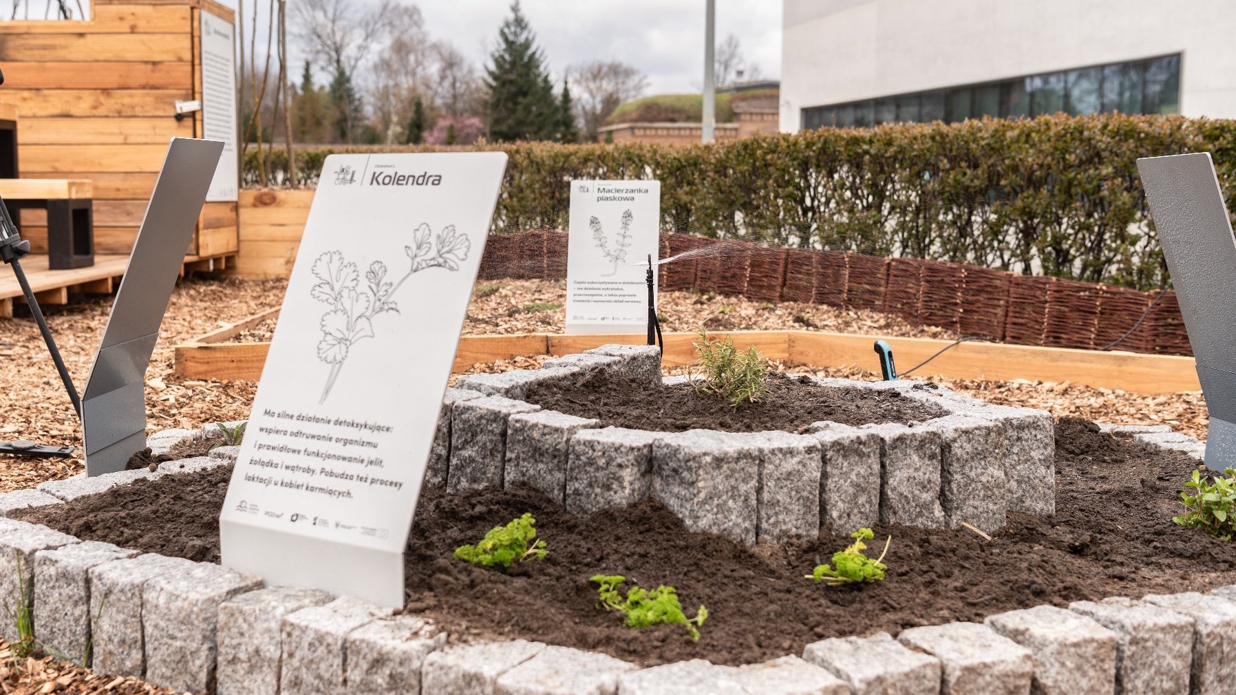 Galeria zdjęć przedstawia ogród eksperymentalny. Widać na nim wydzielone miejsce na rośliny oraz prelegentów konferencji.