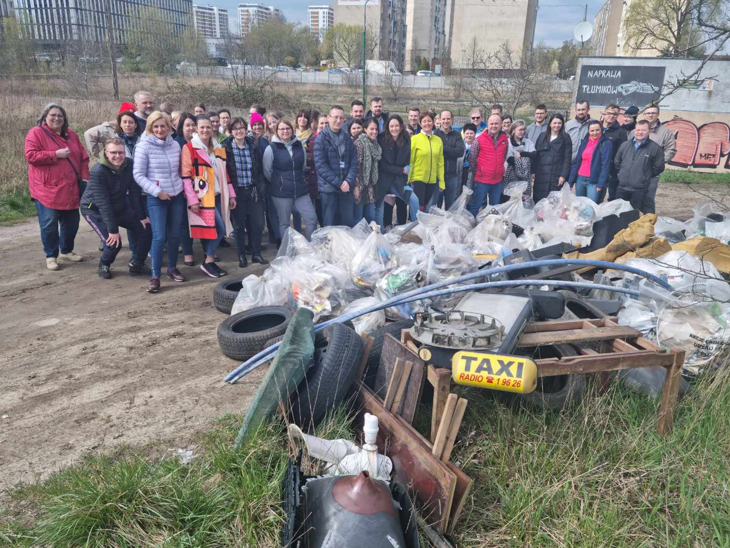 Zdjęcie przedstawia zbiorowe zdjęcie pracowników urzędu. Na pierwszym planie znajduje się góra śmieci. - grafika rozmowy