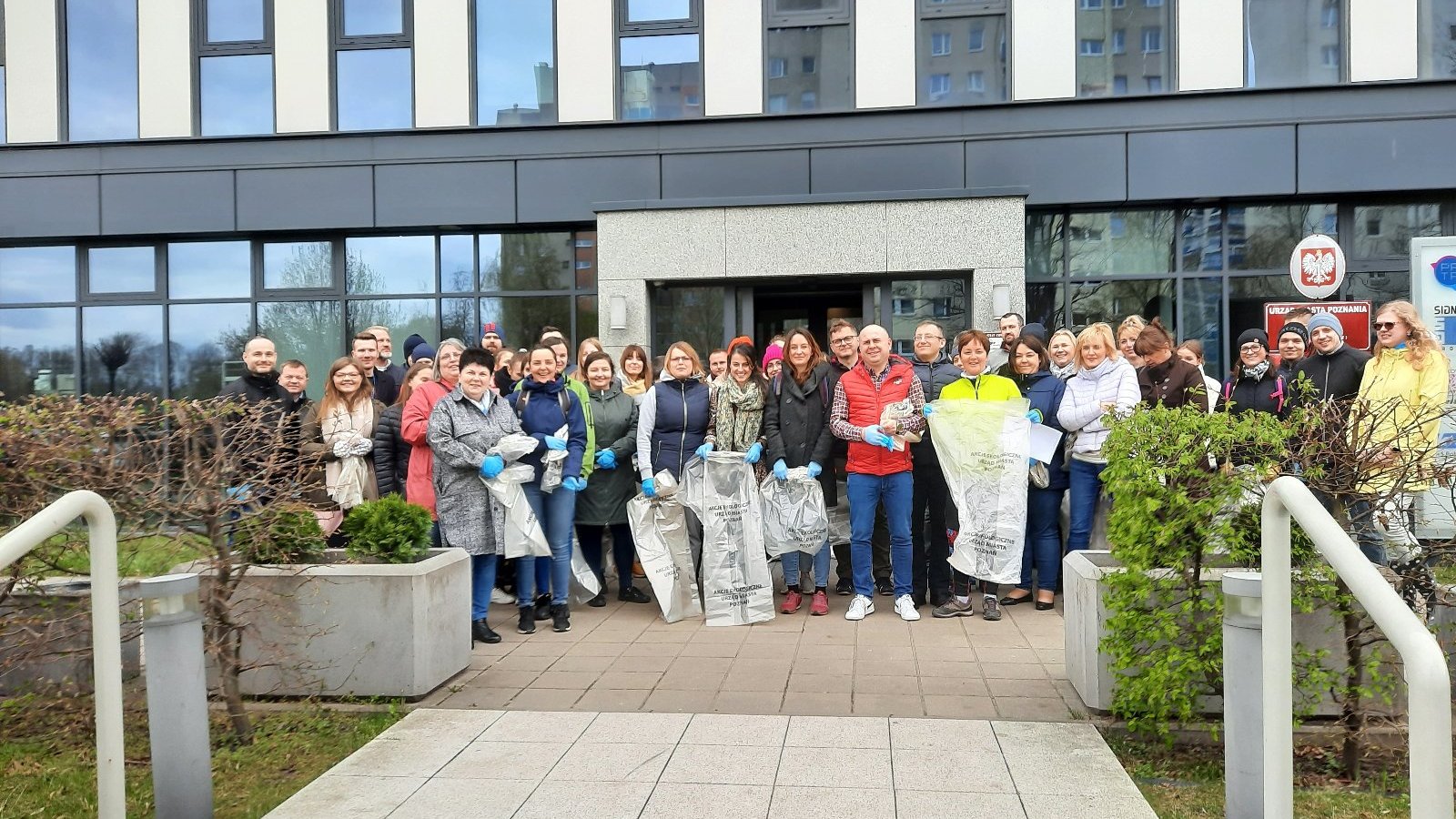 Zdjęcie przedstawia grupowe zdjęcie pracowników urzędu z workami na śmieci.