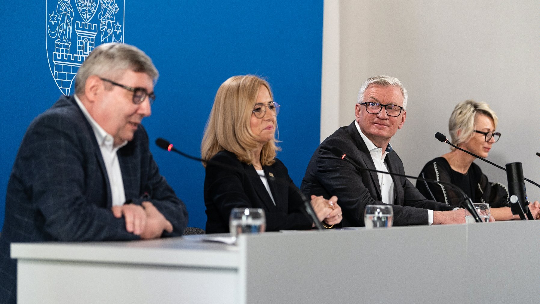 Na zdjęciu cztery osoby za stołem konferencyjnym, w środku prezydent Poznania, w tle granatowa ścianka