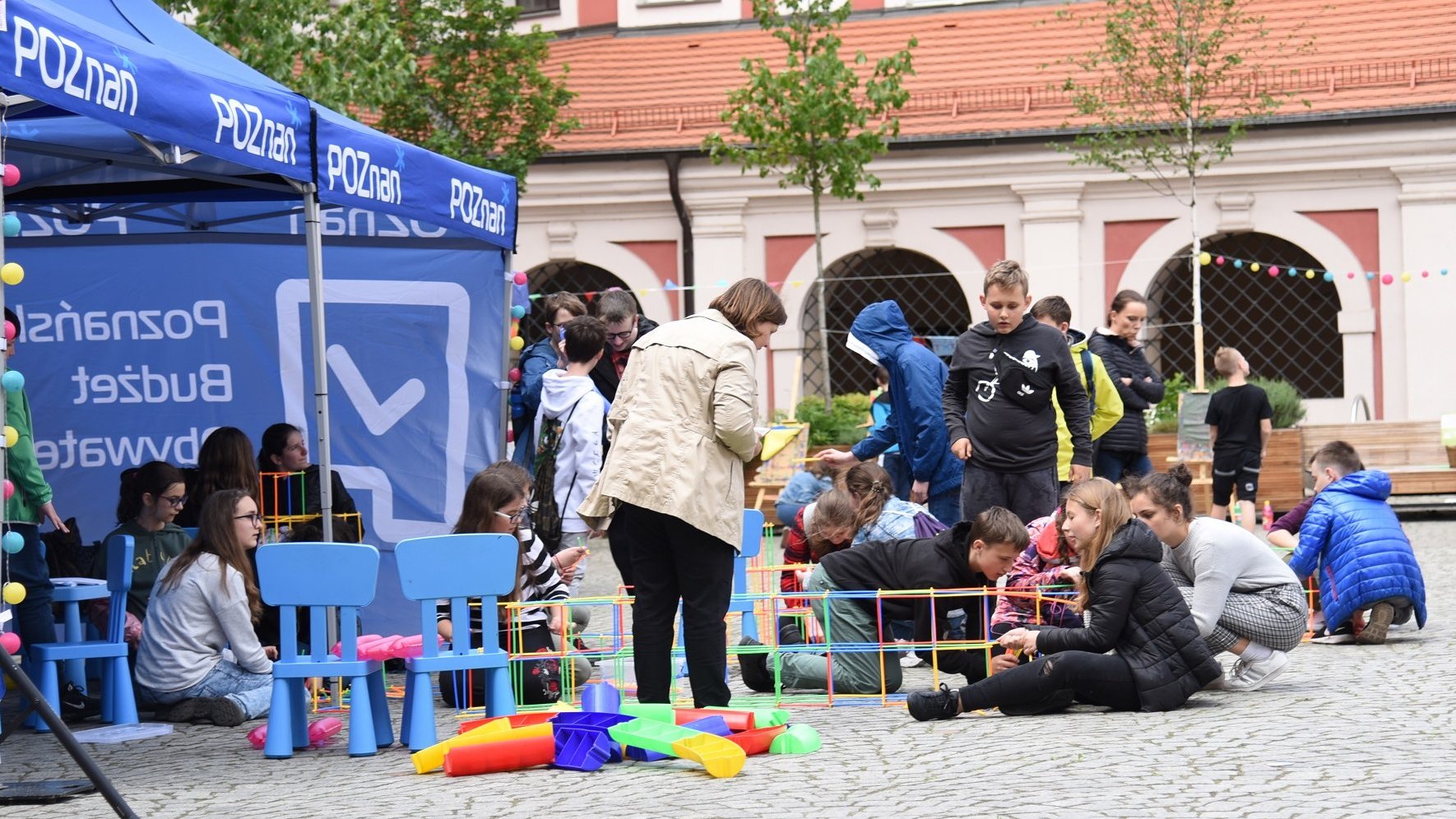 Zdjęcie przedstawia niebieski namiot. Obok znajdują się bawiące się dzieci i młodzież.