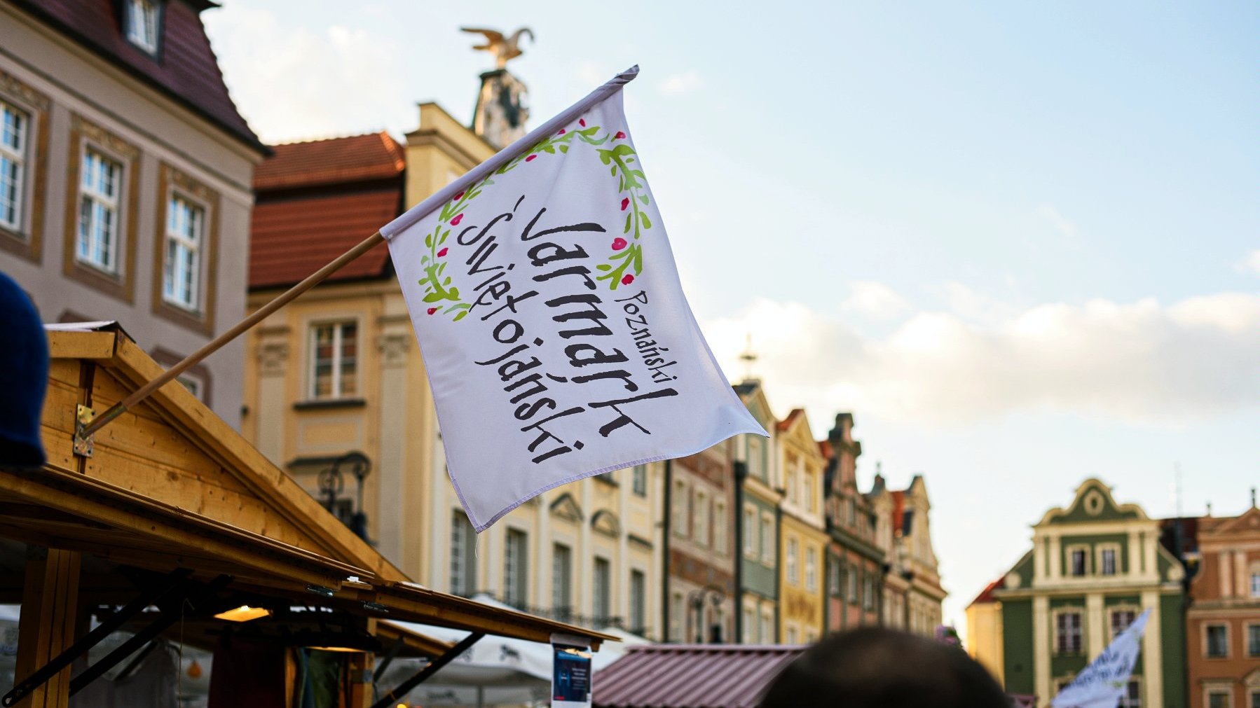 Galeria zdjęć przedstawia tłum ludzi na rynku podczas jarmarku i drewniane domki i stragany z różnymi towarami.