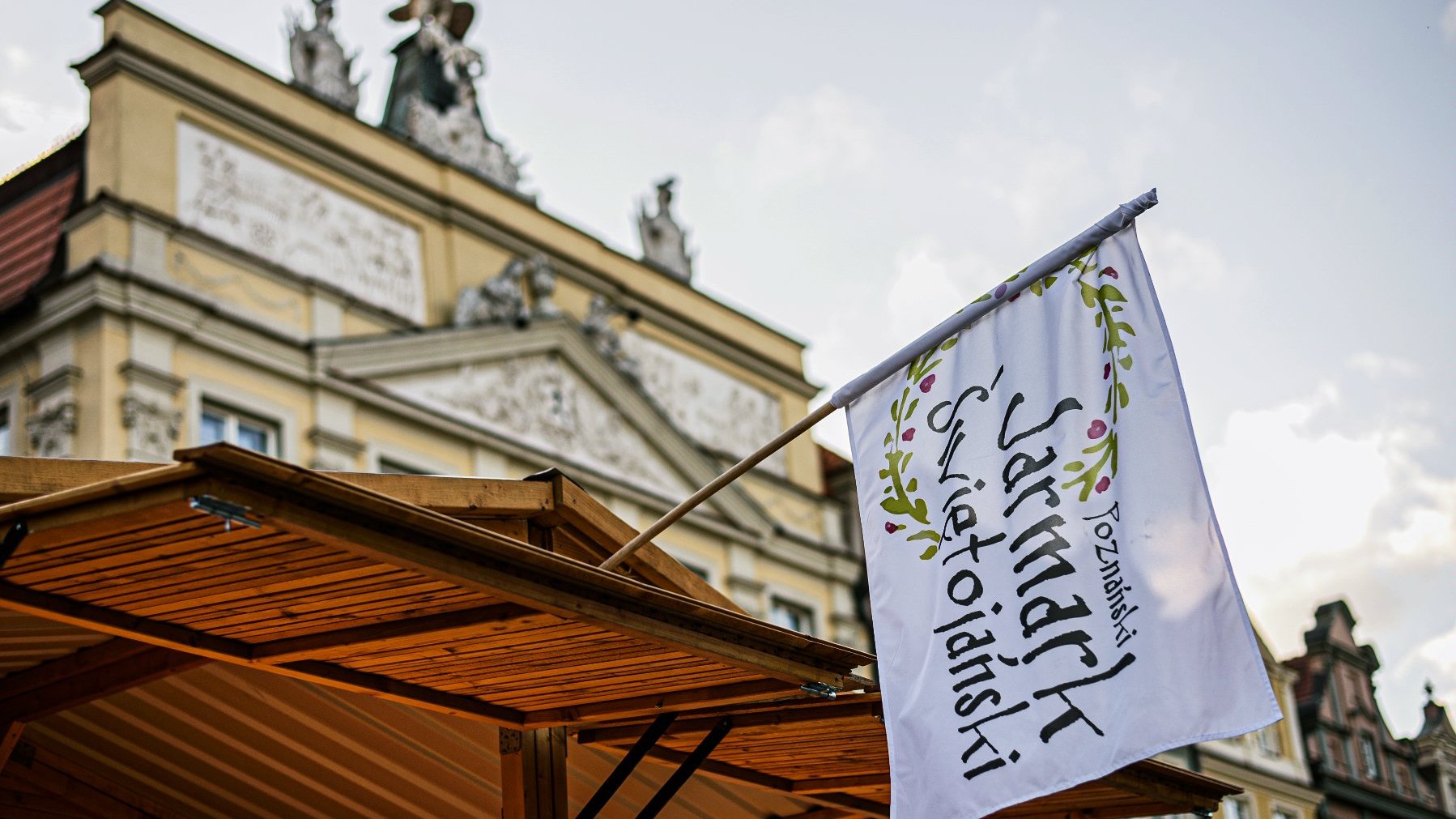 Galeria zdjęć przedstawia tłum ludzi na rynku podczas jarmarku i drewniane domki i stragany z różnymi towarami.