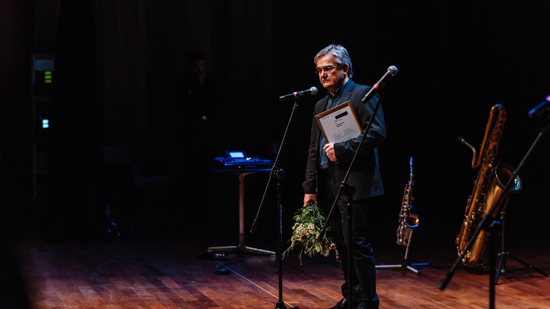 Na zdjęciu laureat Nagrody stojący przed mikrofonem, w ręku trzyma kwiaty