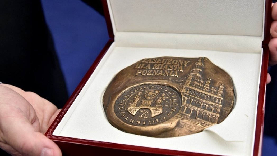 Na zdjęciu medal "Zasłużony dla Miasta Poznania" w pudełku, trzymany w dłoniach - grafika rozmowy