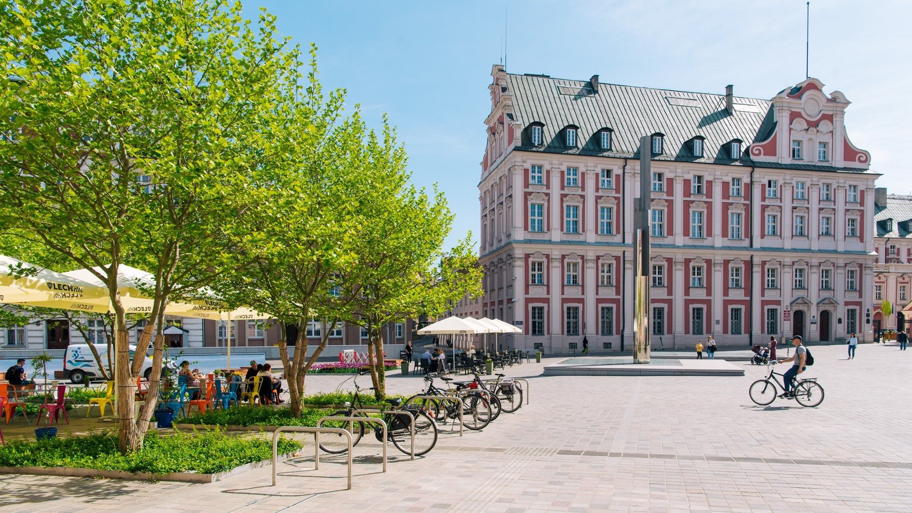 Na zdjęciu pl. Kolegiacki.Po lewej ogródek restauracyjny otoczony drzewami. Po prawej budynek urzędu miasta.